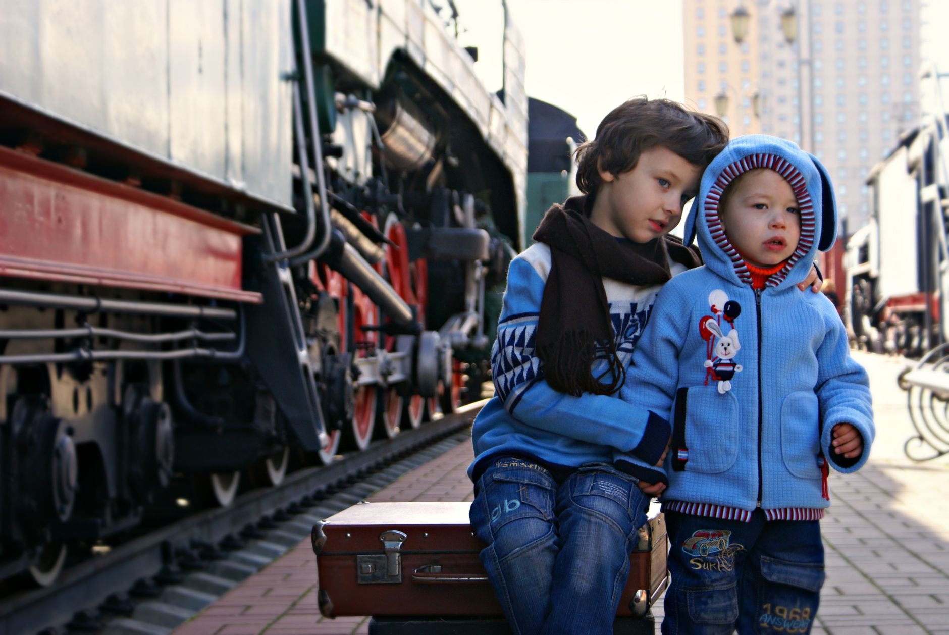 Two young boys sitting by a vintage train, waiting at the station.
