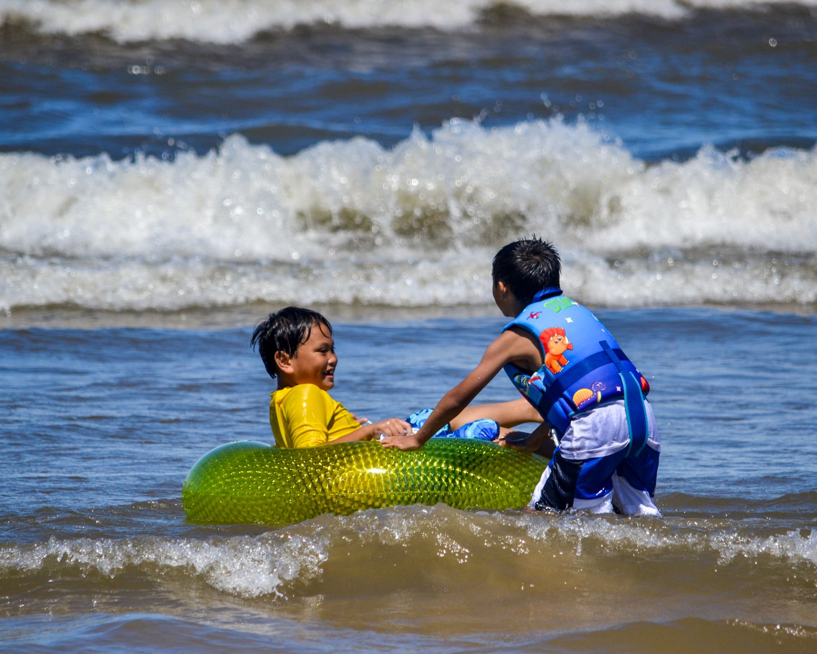 Two children enjoy a summer day at the beach with a colorful inflatable ring.