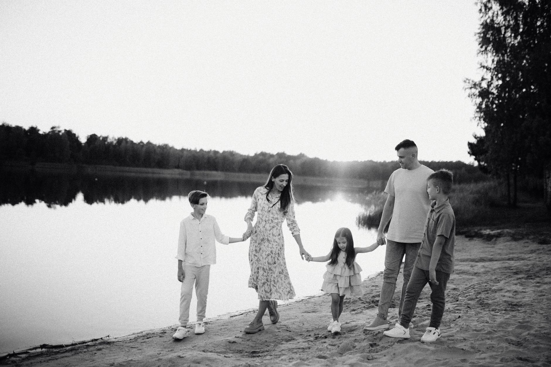 Monochrome photo of a family walking hand in hand along a serene lakeshore.