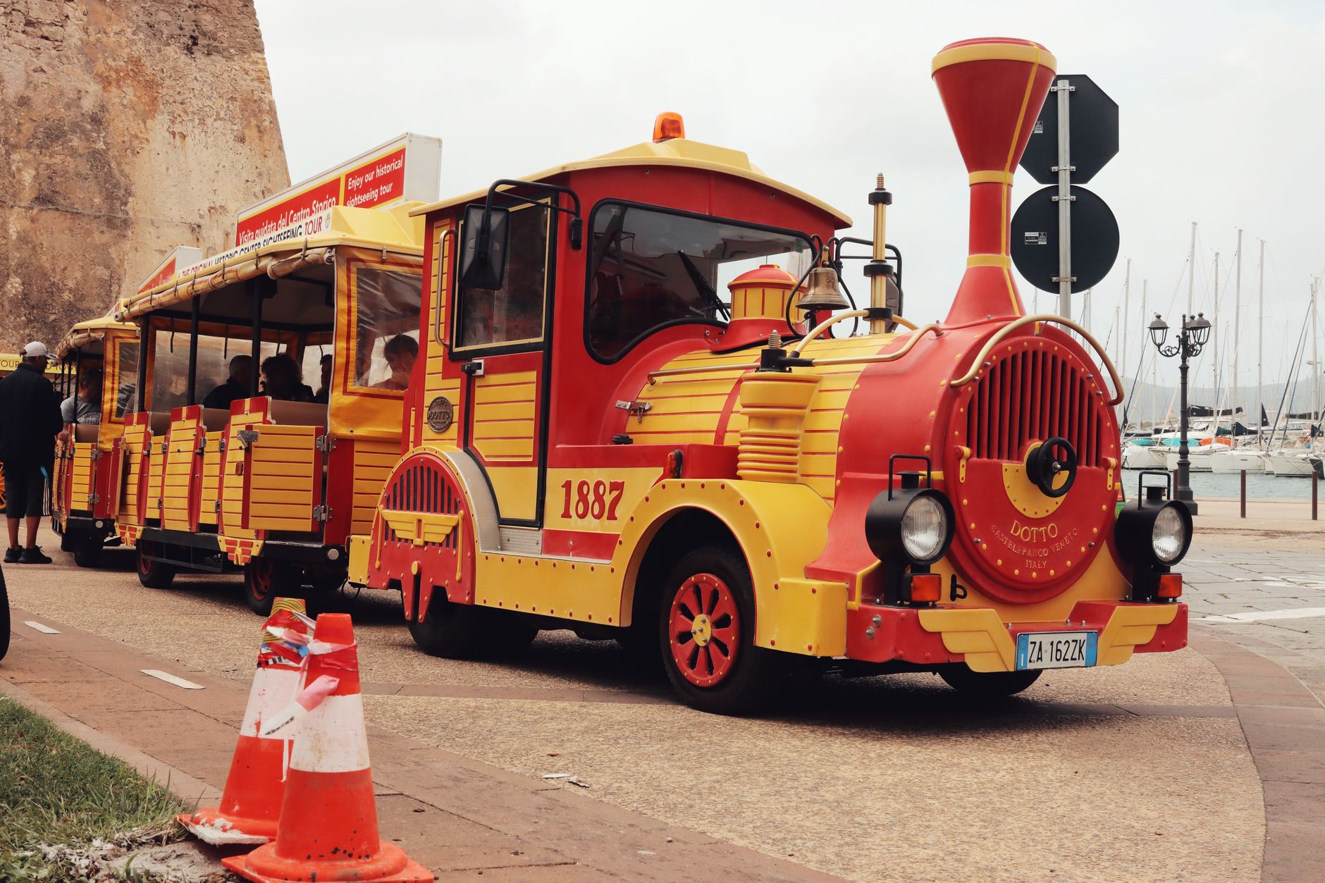 A vibrant tourist train with vintage design on Alghero's streets, Sardinia, Italy.