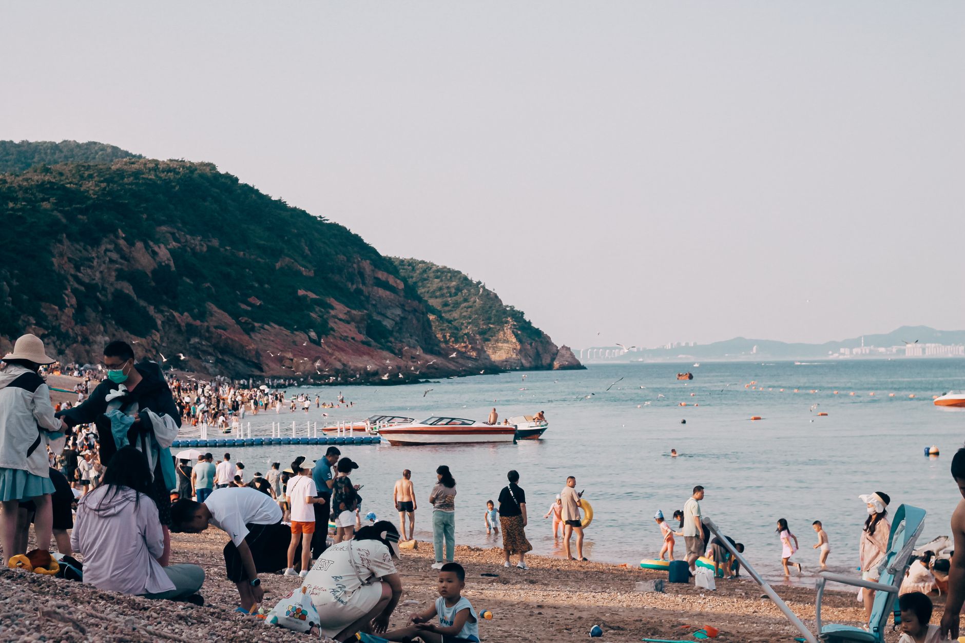 A lively beach scene with families enjoying the shore and boats on the water.