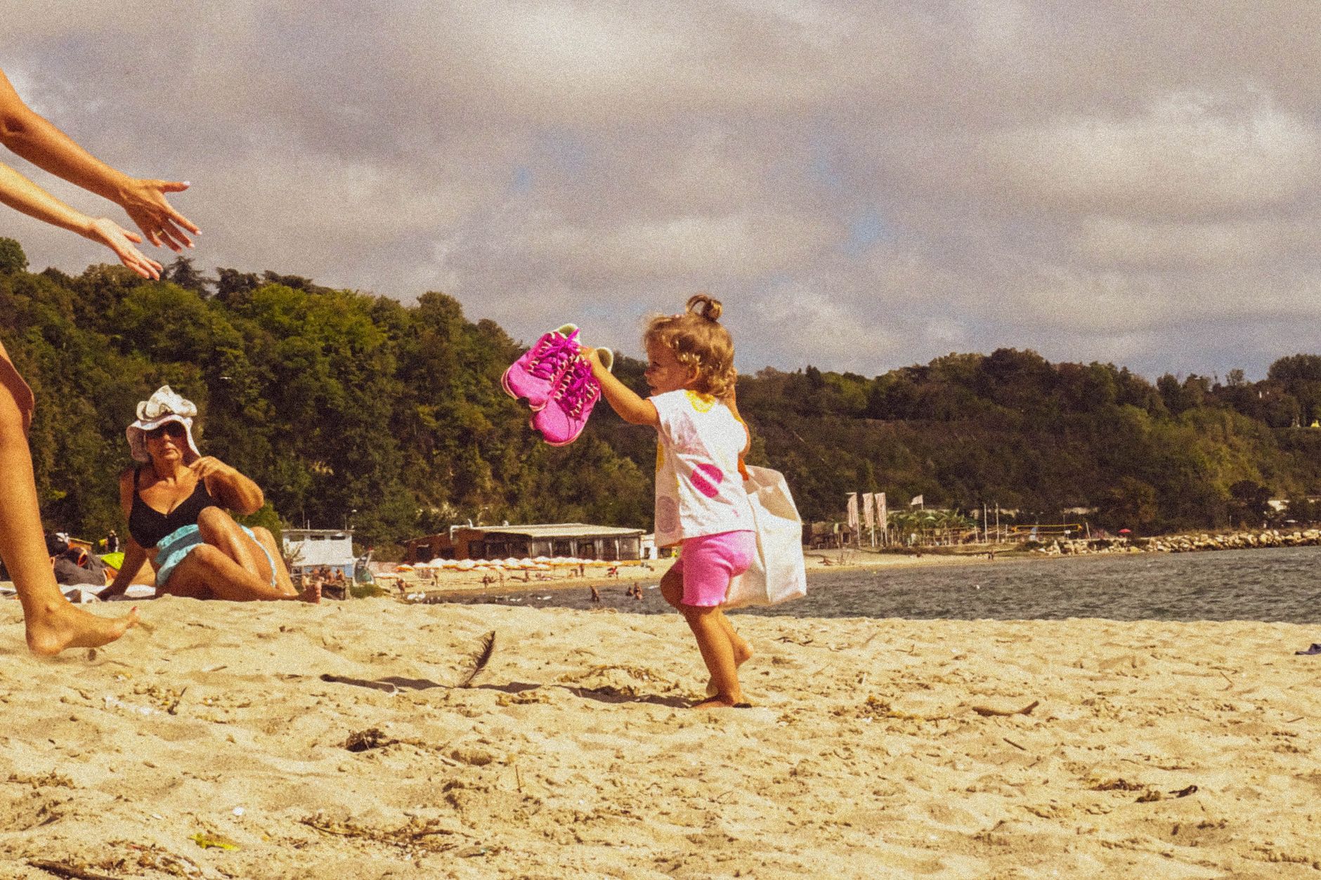 A playful child runs on a sunny beach towards waiting arms, showcasing family fun.