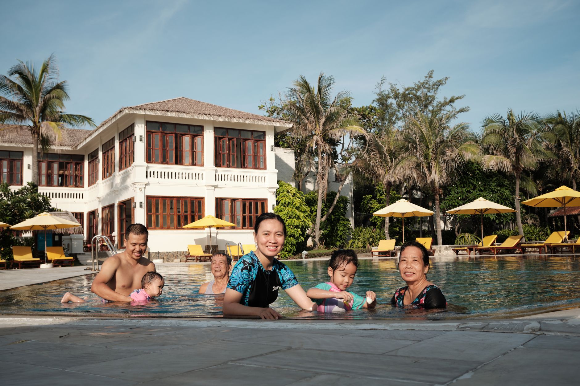 Happy Asian family enjoying a sunny day by the pool at a luxurious resort.