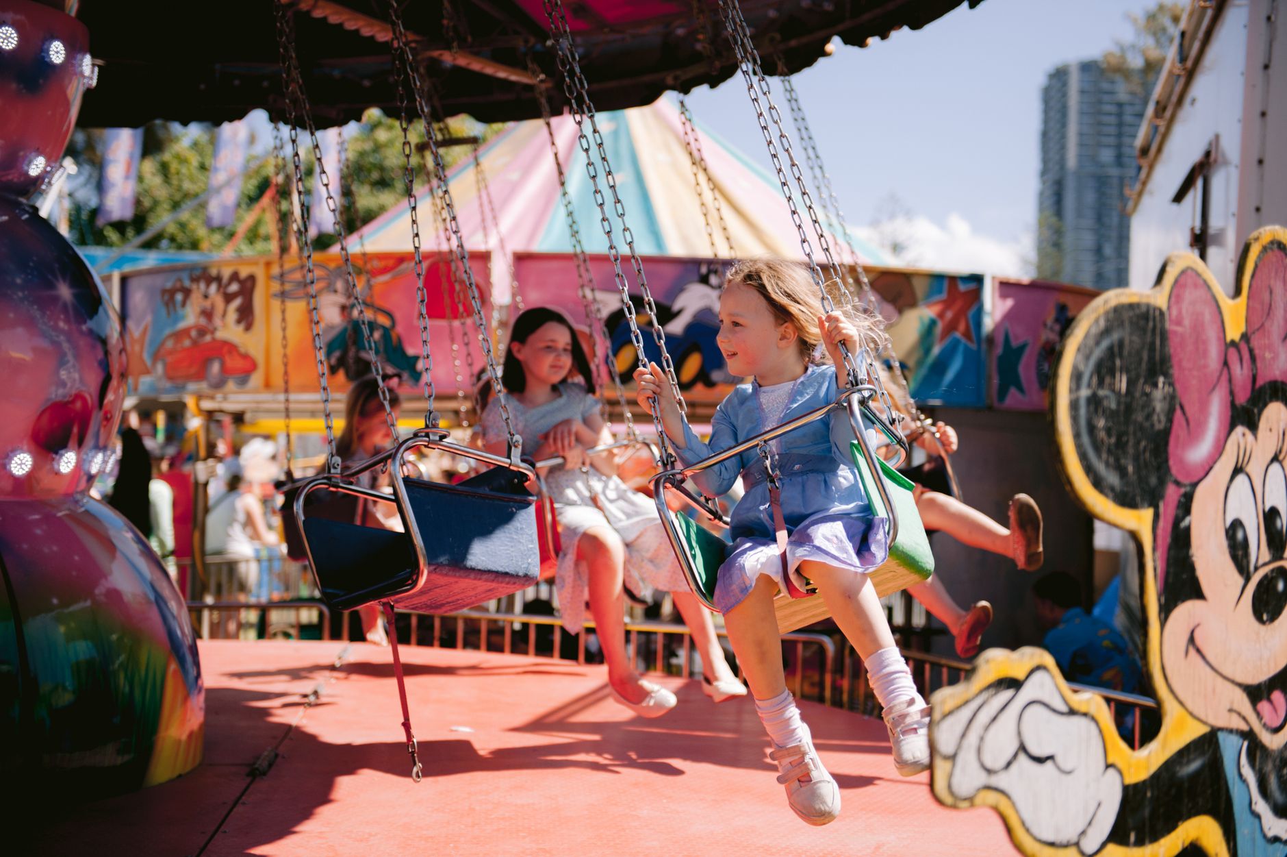 Joyful children on swings at carnival, enjoying a sunny day filled with laughter and fun.