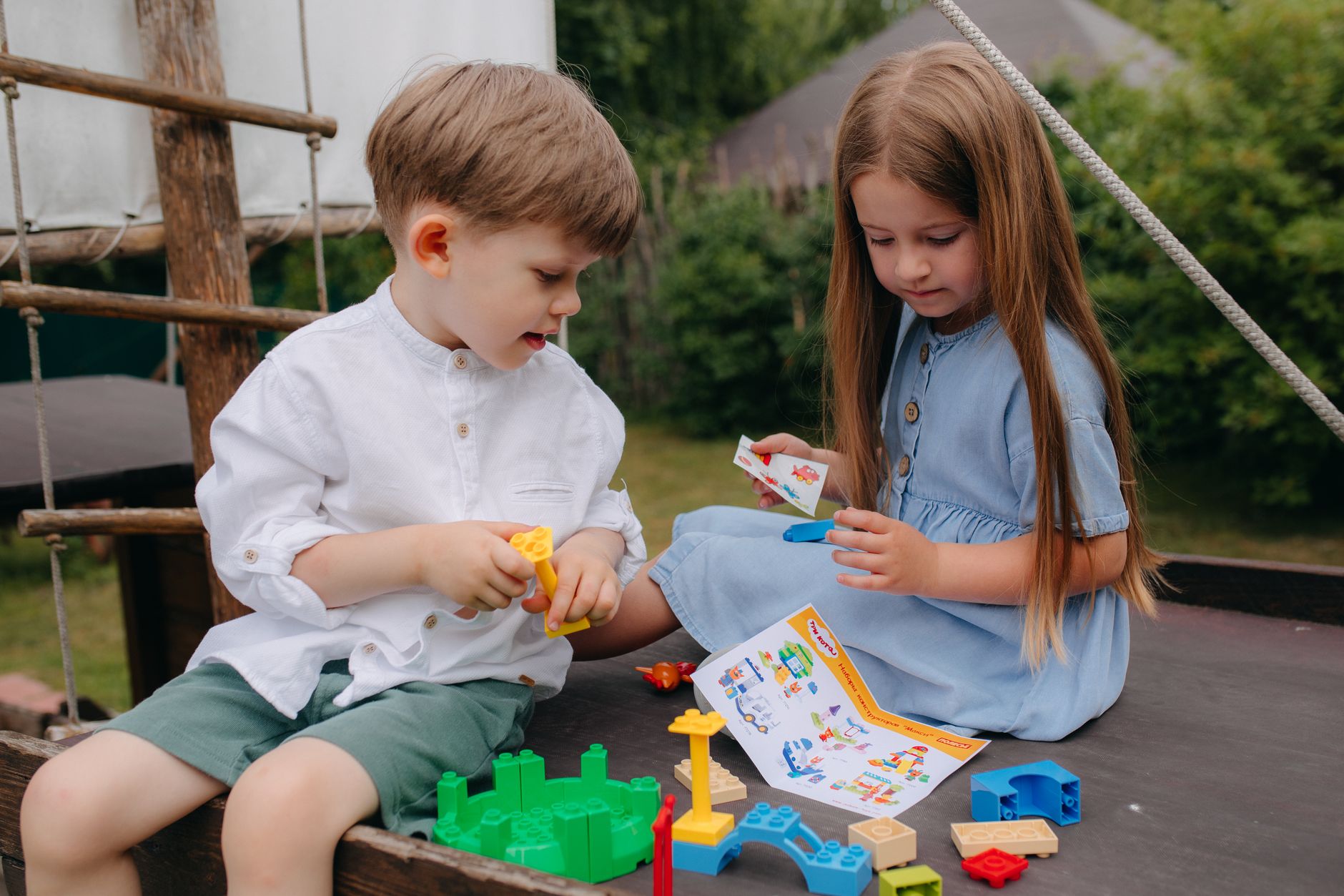 Two children enjoy playing with colorful building blocks on a sunny day.