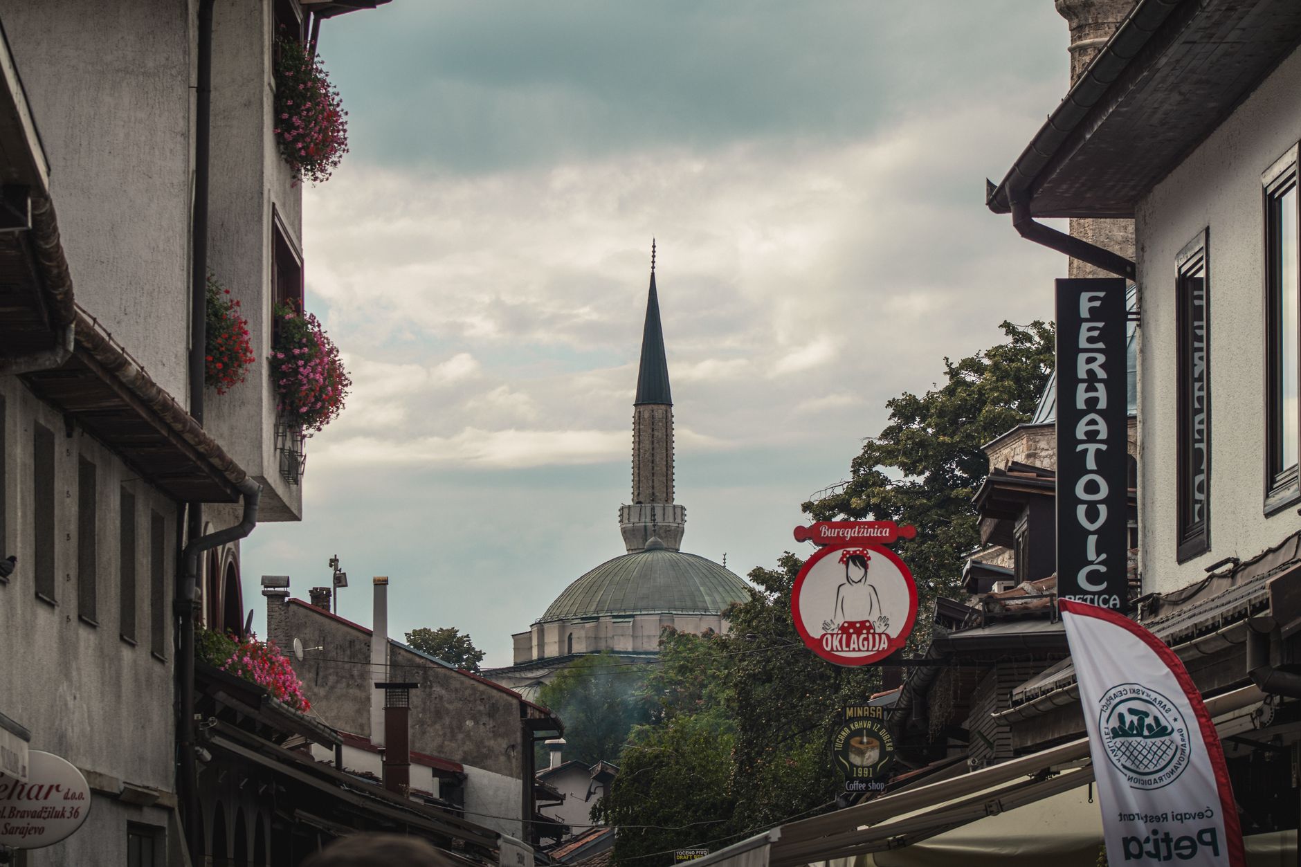 Charming view of Sarajevo street with historical mosque in the background and vibrant signage.