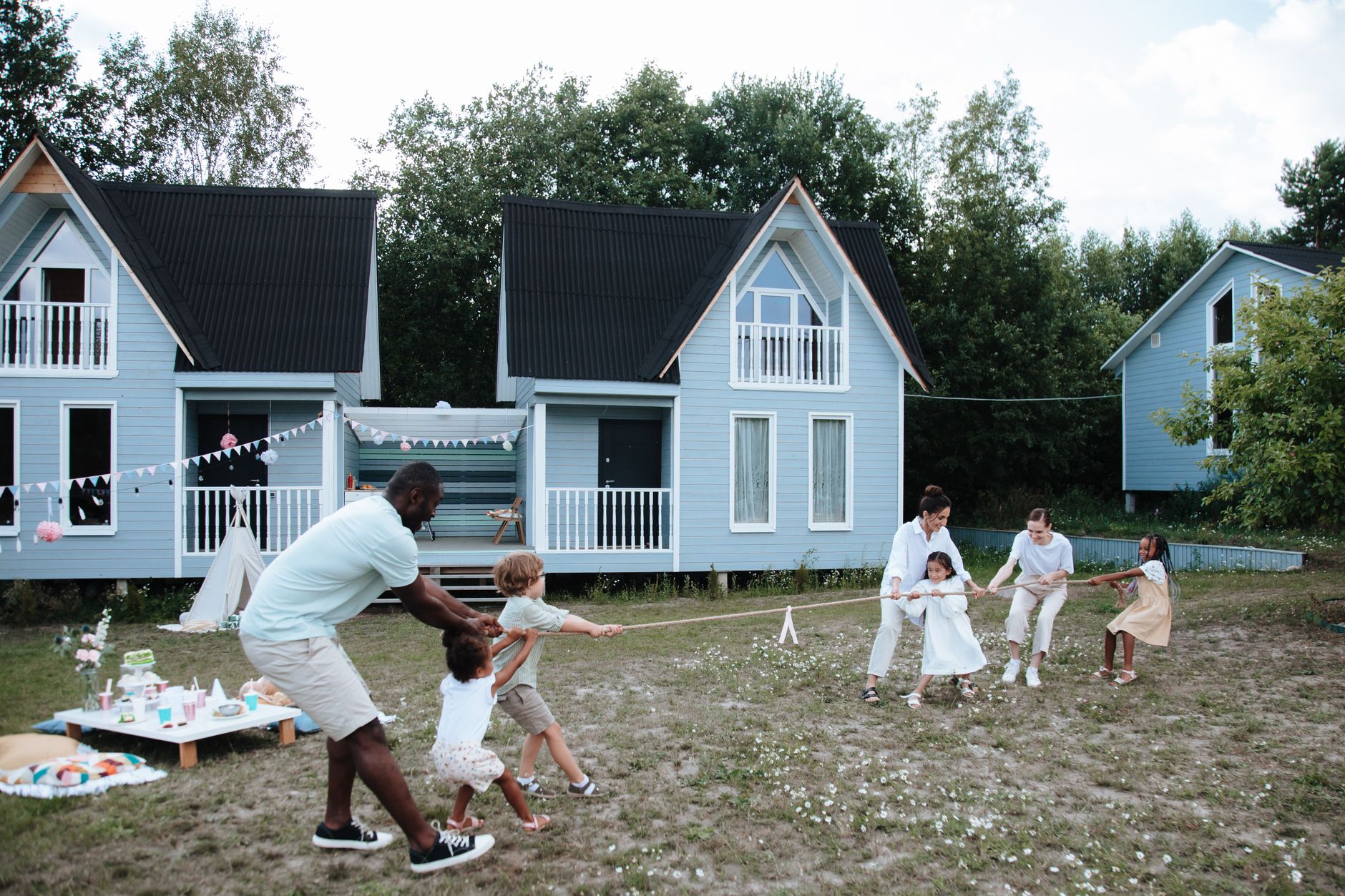 A diverse family plays tug of war outdoors near modern houses, enjoying a sunny day.