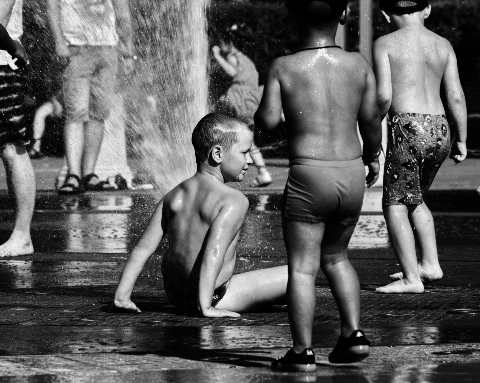 Black and white image of kids enjoying a water fountain. Captures playful summer vibes.