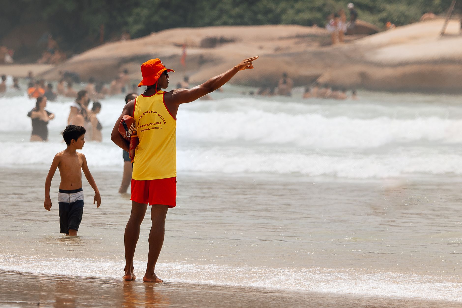 A vigilant lifeguard aids a child on a crowded summer beach, ensuring safety.