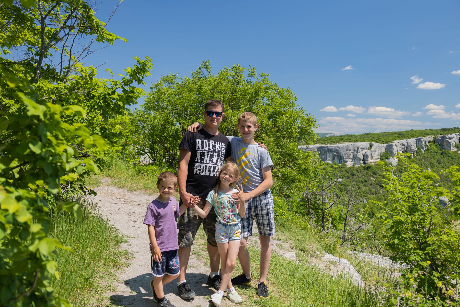 Father and children enjoying a sunny day hike with picturesque cliff backdrop.