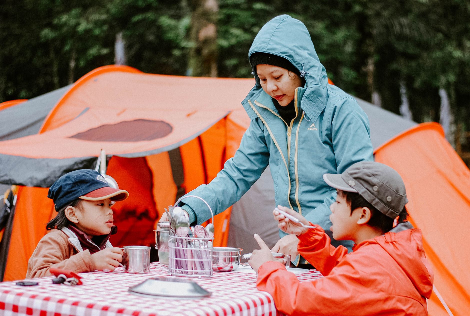 Mother serving food to her children at a campsite with orange tents in the background.