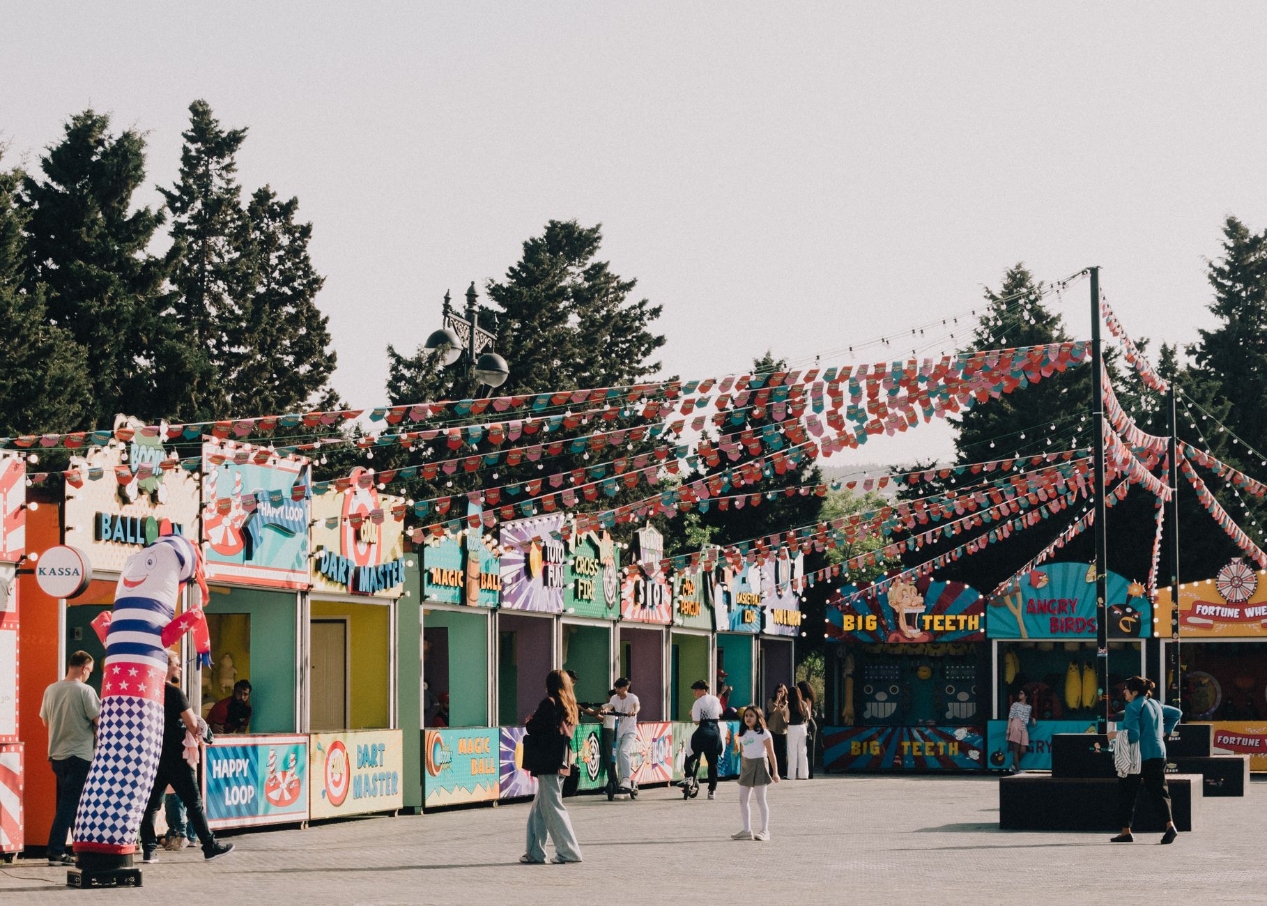 Vibrant outdoor carnival scene with colorful stalls, bunting, and people enjoying the festive atmosphere.