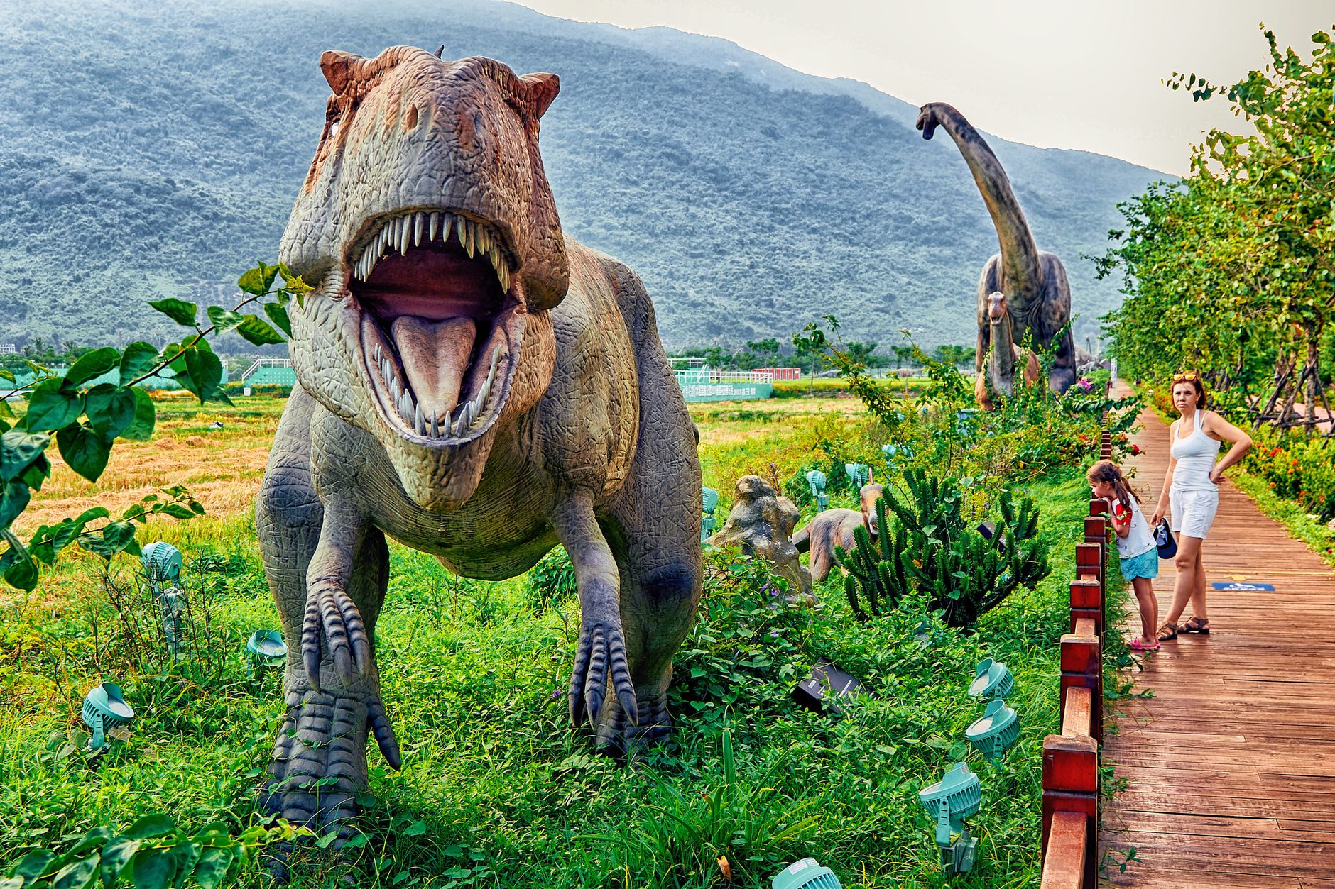 Vibrant dinosaur park scene featuring lifelike sculptures and visitors exploring the park.