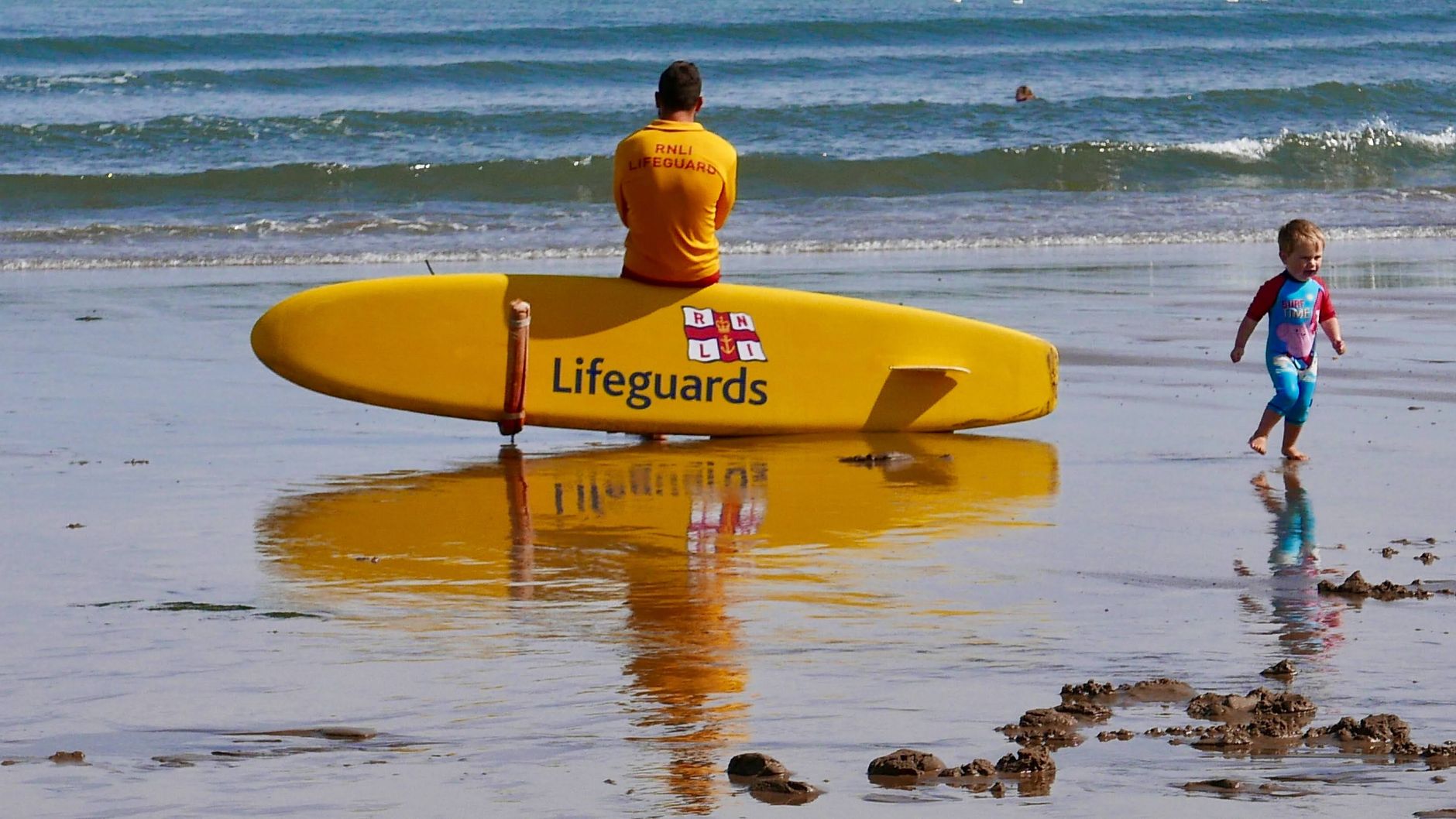 Lifeguard watching over Saltburn beach with a child playing nearby on a sunny summer day.