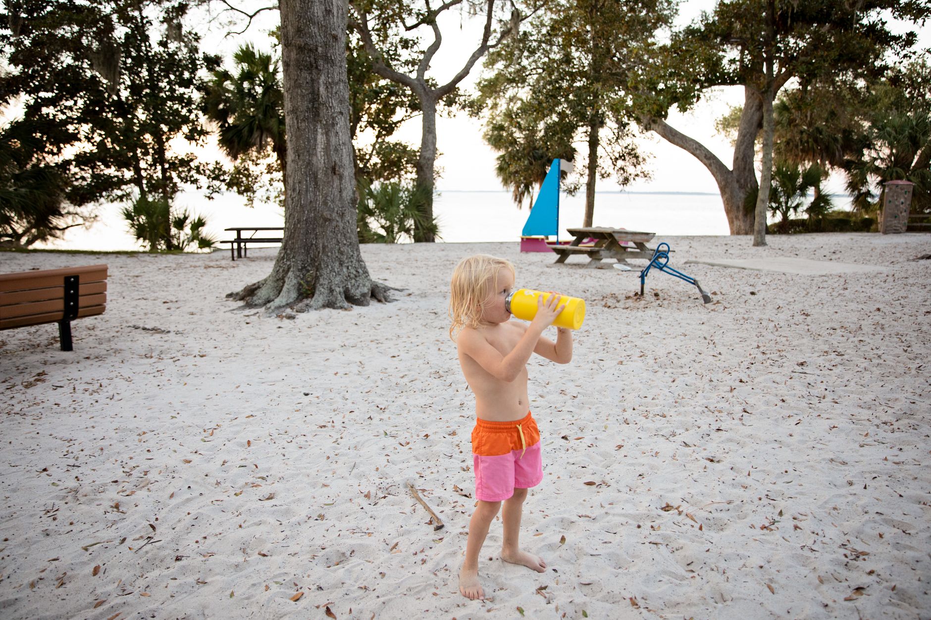 A young child drinks from a water bottle on a sandy beach at Hilton Head Island.