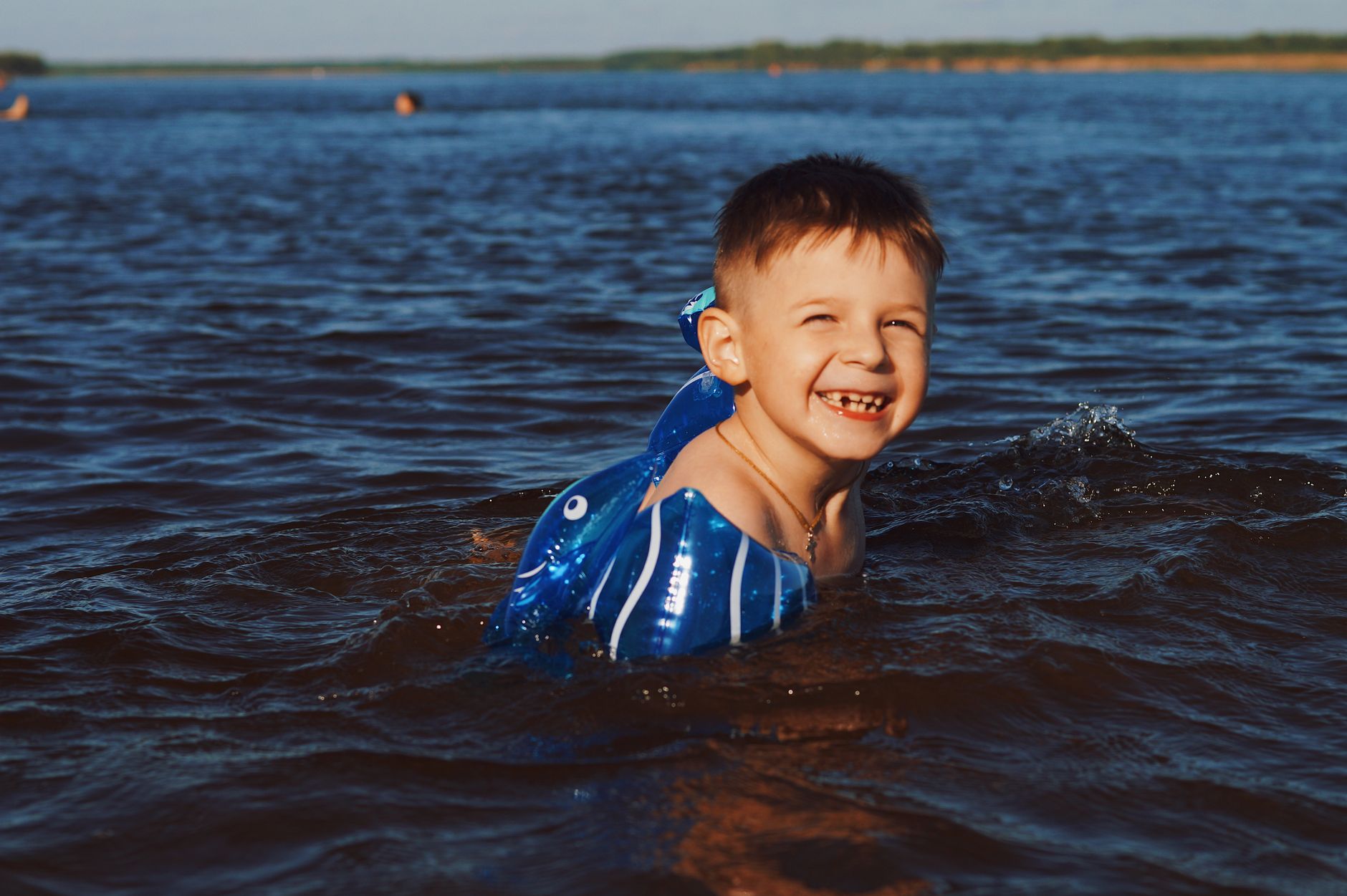 A happy child swimming with inflatable floats in a sunny lake, enjoying a summer day.