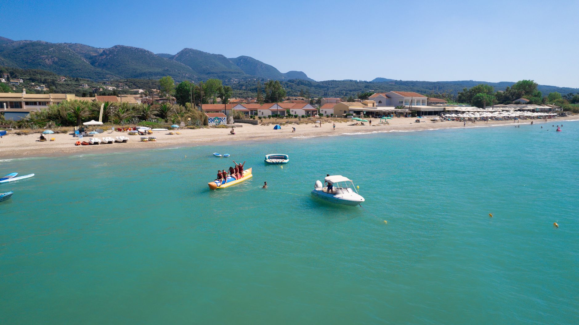 Turquoise sea and vibrant beach scene in Corfu, Greece, capturing summer fun and water activities.