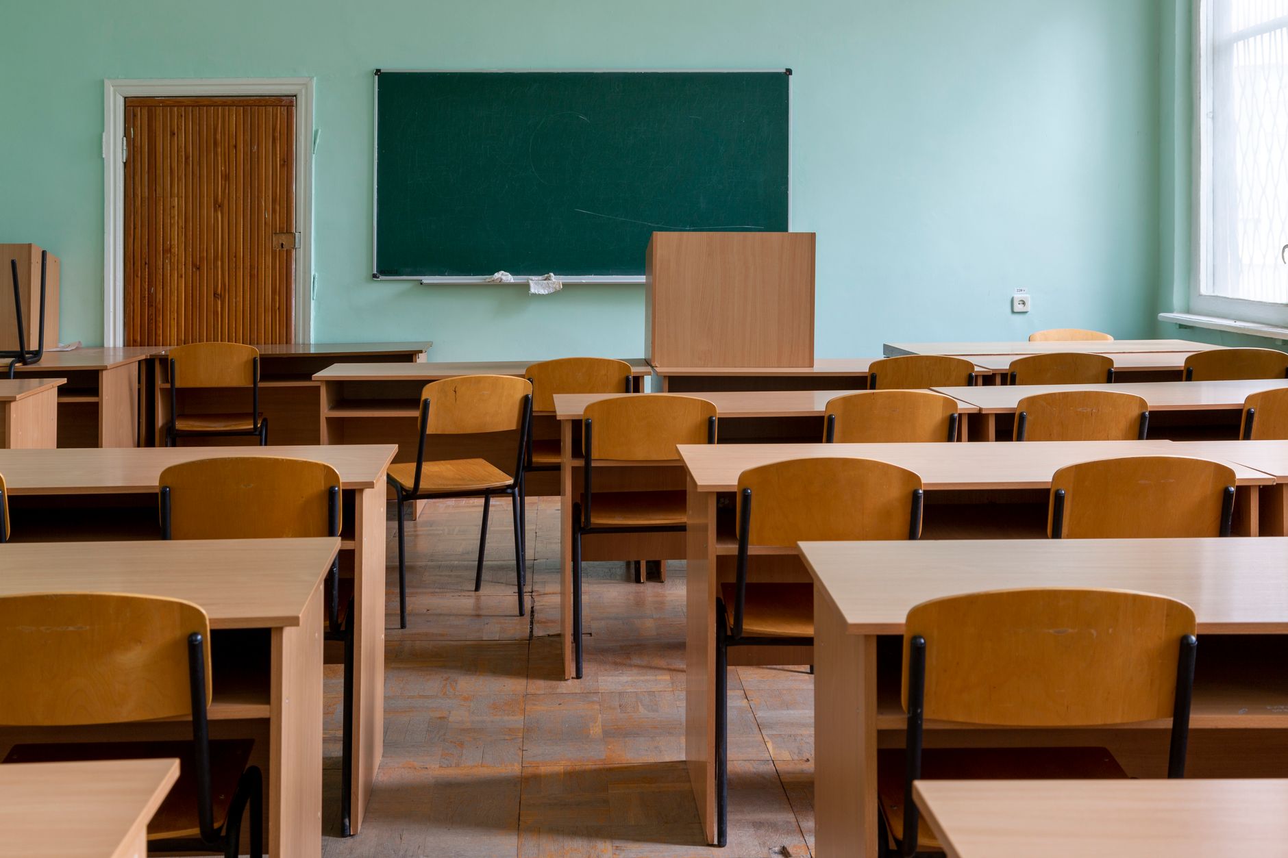 An empty classroom featuring wooden desks, chairs, and a large green chalkboard.