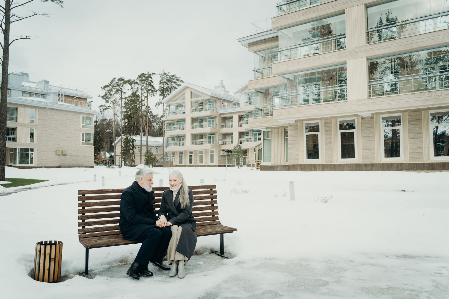 Senior couple holding hands on a bench in snowy winter setting.