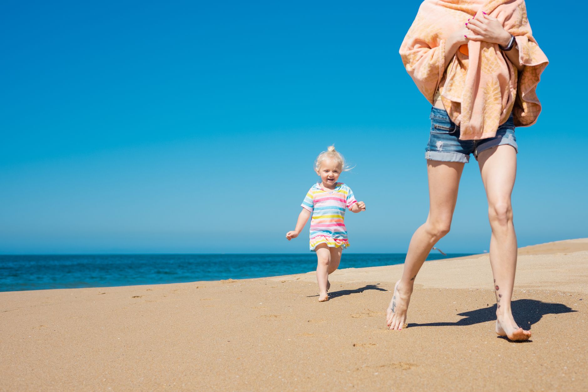 A cheerful mother and daughter running on a sunny beach, having fun together.
