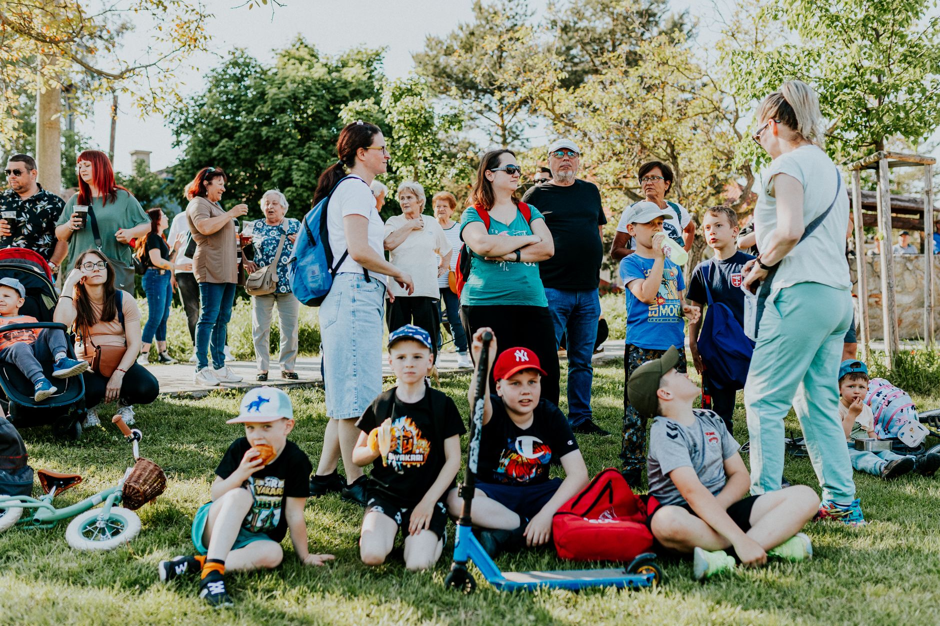 A diverse group of families and children enjoying an outdoor event on a sunny day in a park setting.