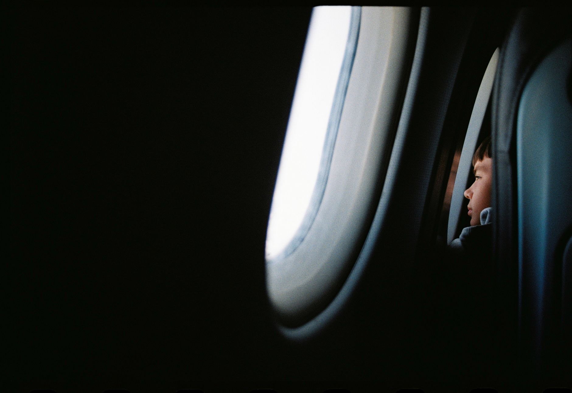 A young boy looking out the airplane window during a flight, capturing the wonder of travel from a child's perspective.