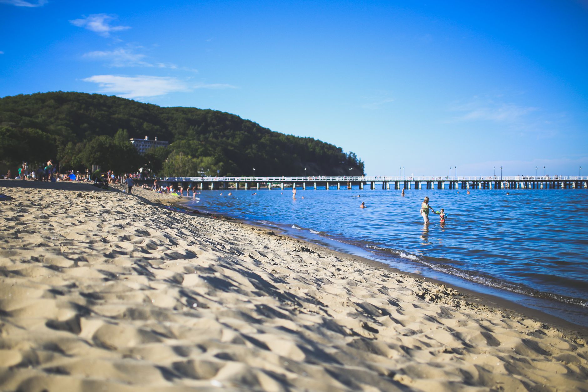 Families enjoy a beautiful summer day at a sandy beach with clear blue skies and gentle waves.