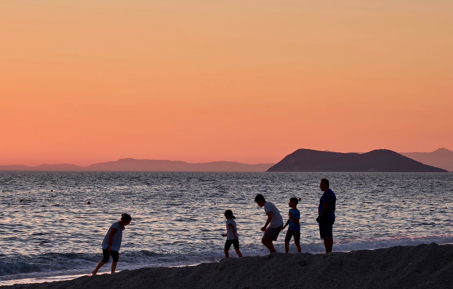 A family enjoying a sunset by the beach at Perdika, Greece, with orange skies and serene waves.