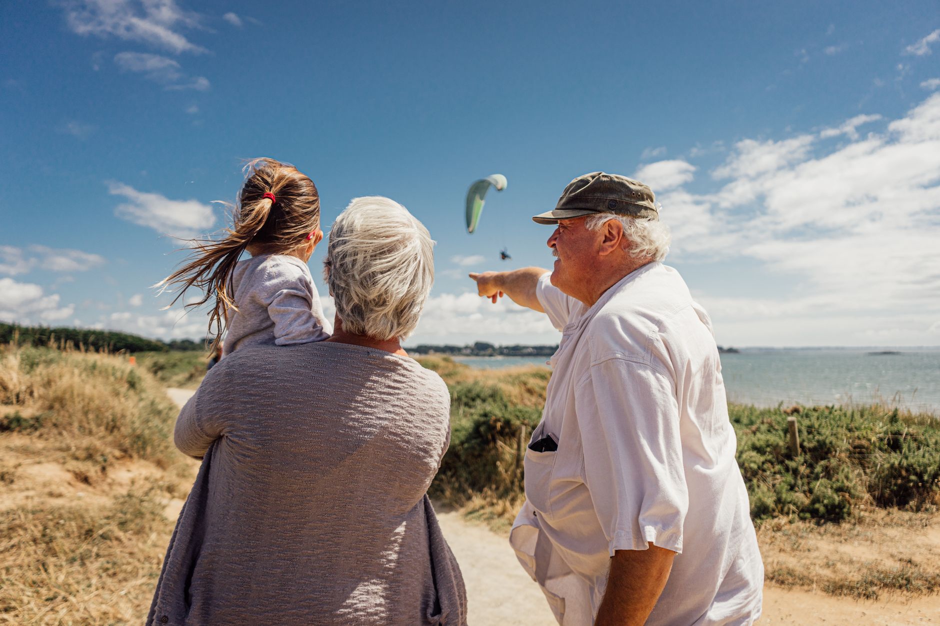 Elderly couple with granddaughter watching the sea and a paraglider on a sunny day in Pénestin, Brittany, France.
