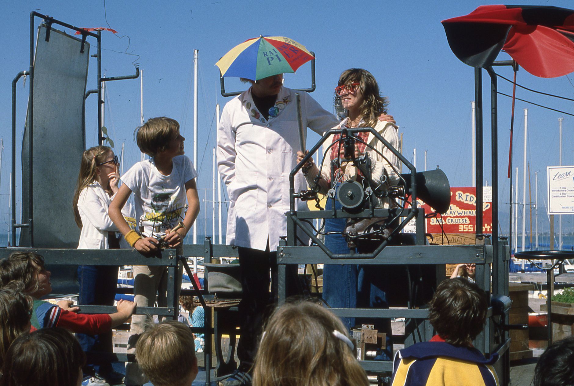A fun summer festival with children enjoying a performance on an outdoor stage.