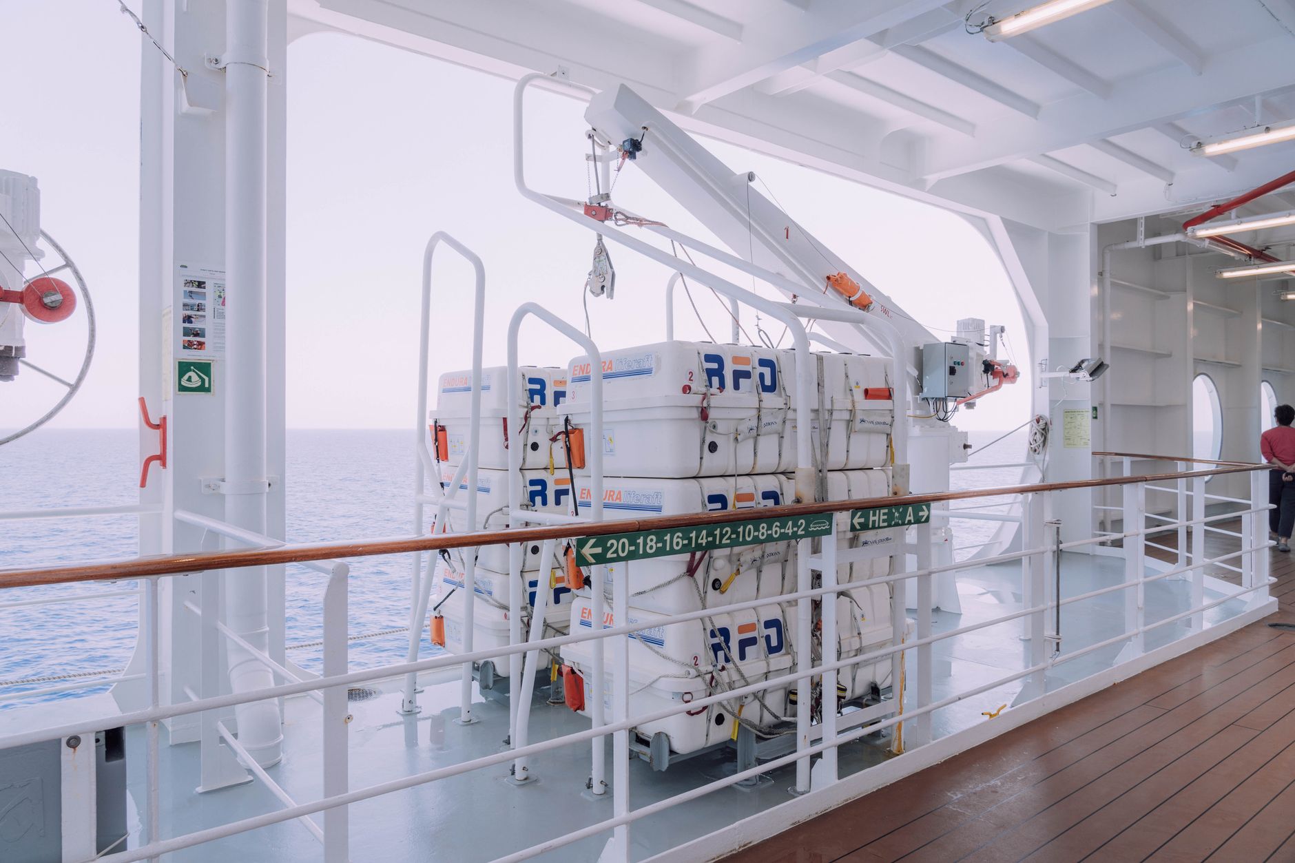 Cruise ship deck with lifeboats and safety equipment overlooking the serene ocean.
