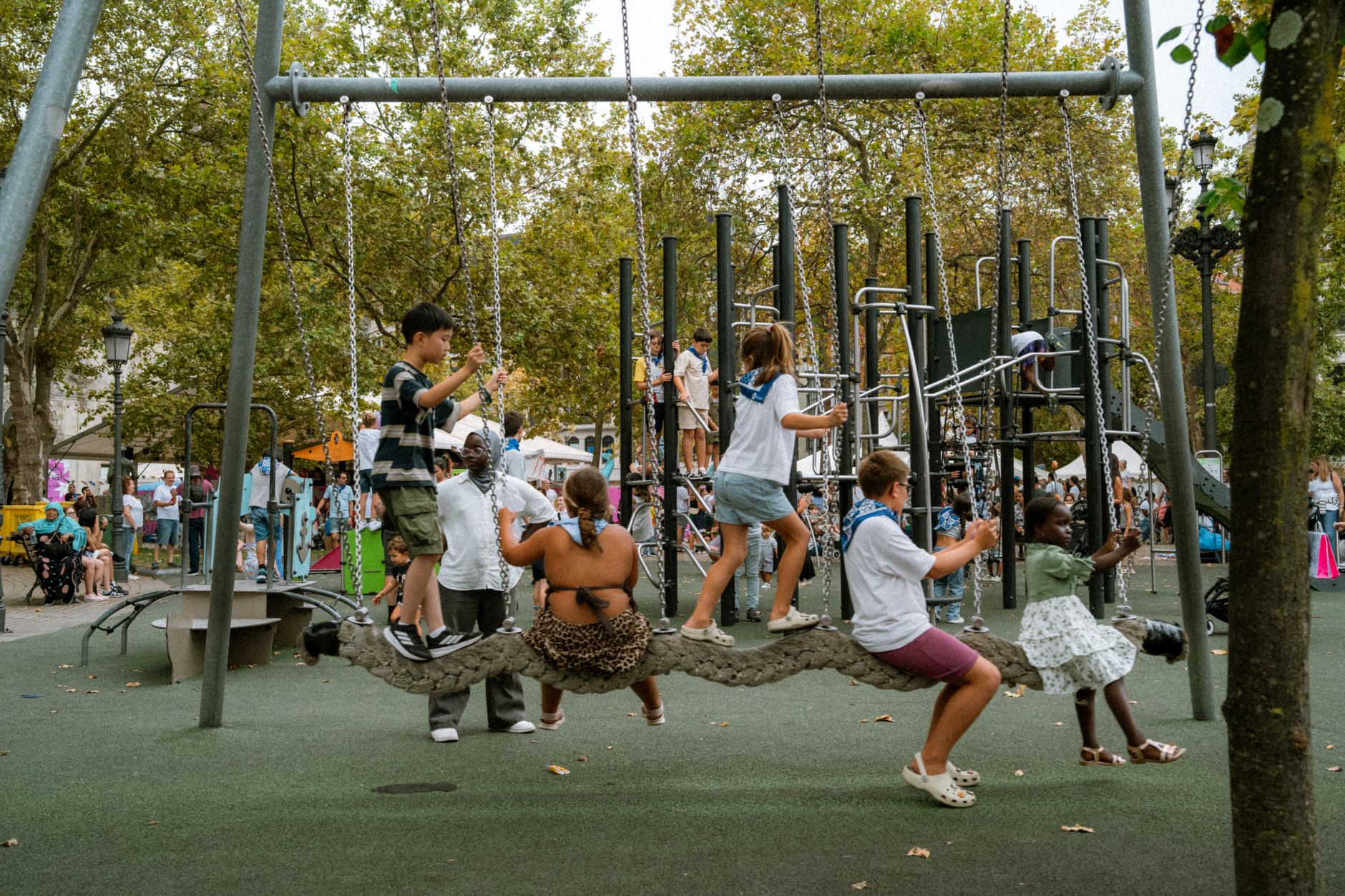 Diverse group of children enjoying a sunny day on a playground with a rope swing.