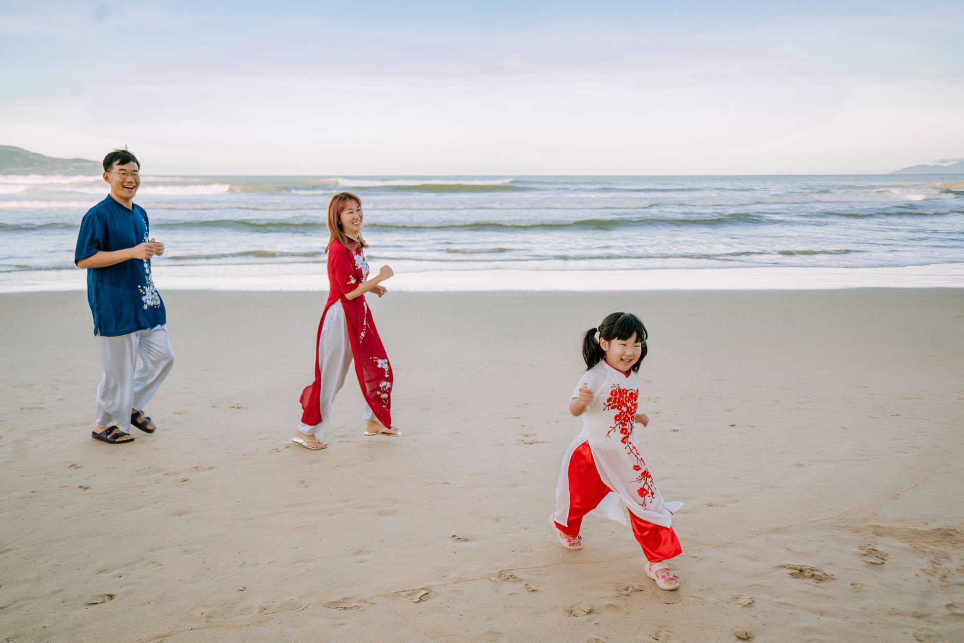 Asian family laughing and playing on a sandy beach during the day.