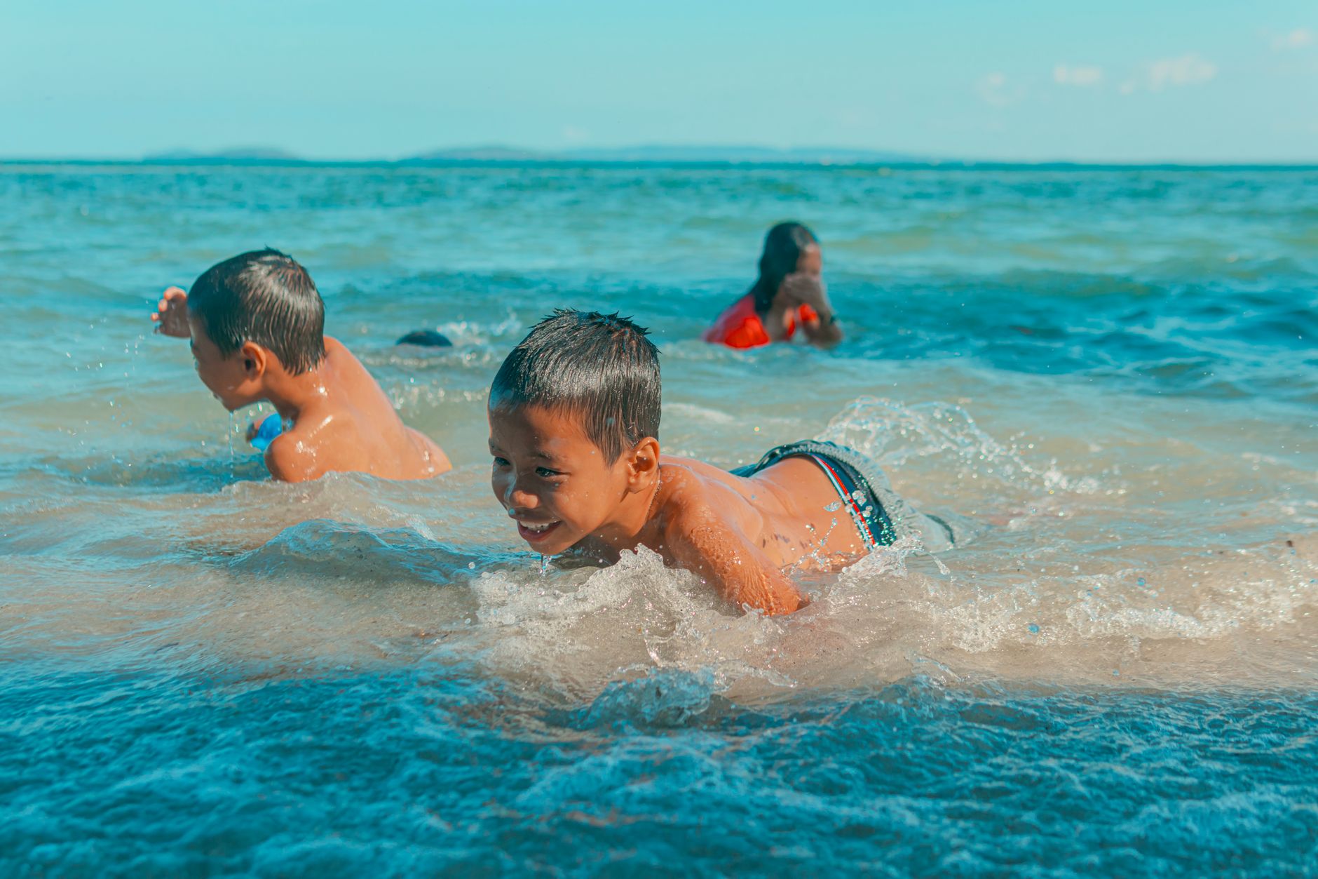 Children swimming and playing in clear sea waves on a sunny day, radiating joy and leisure.