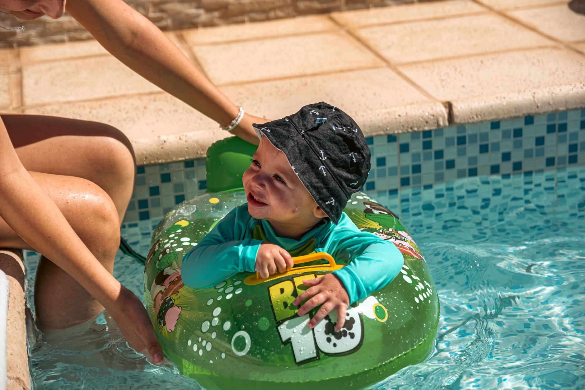 Adorable baby in a float enjoying a sunny pool day while being supported by an adult.
