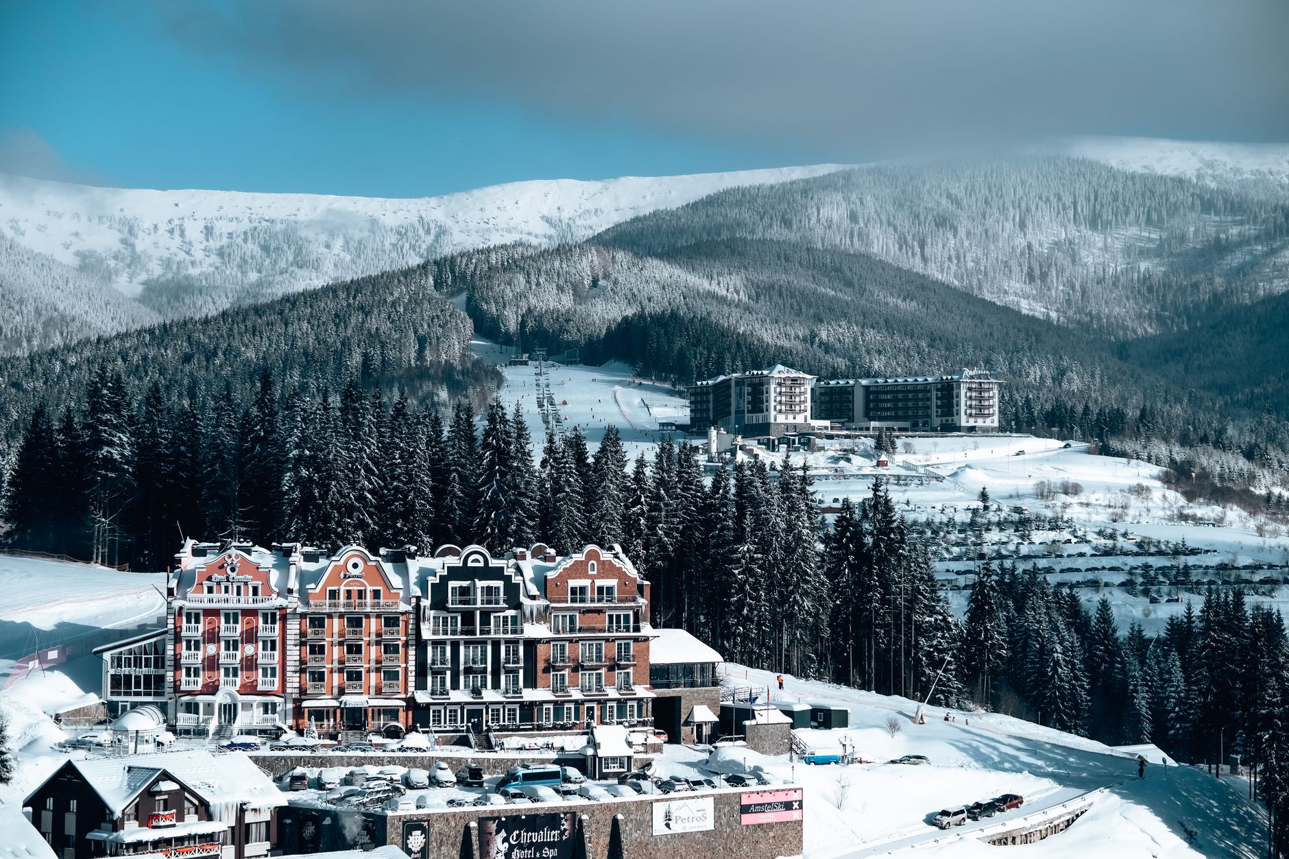 Charming hotel buildings nestled in a snowy mountain landscape with evergreen trees and clear skies.
