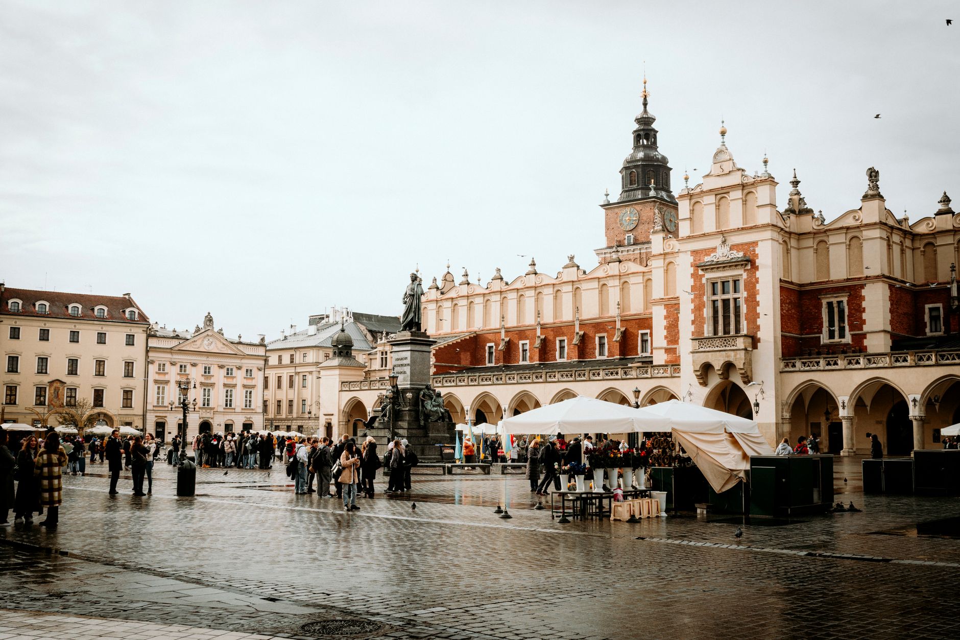 Bustling scene at Kraków's historic Market Square with Cloth Hall and statue.