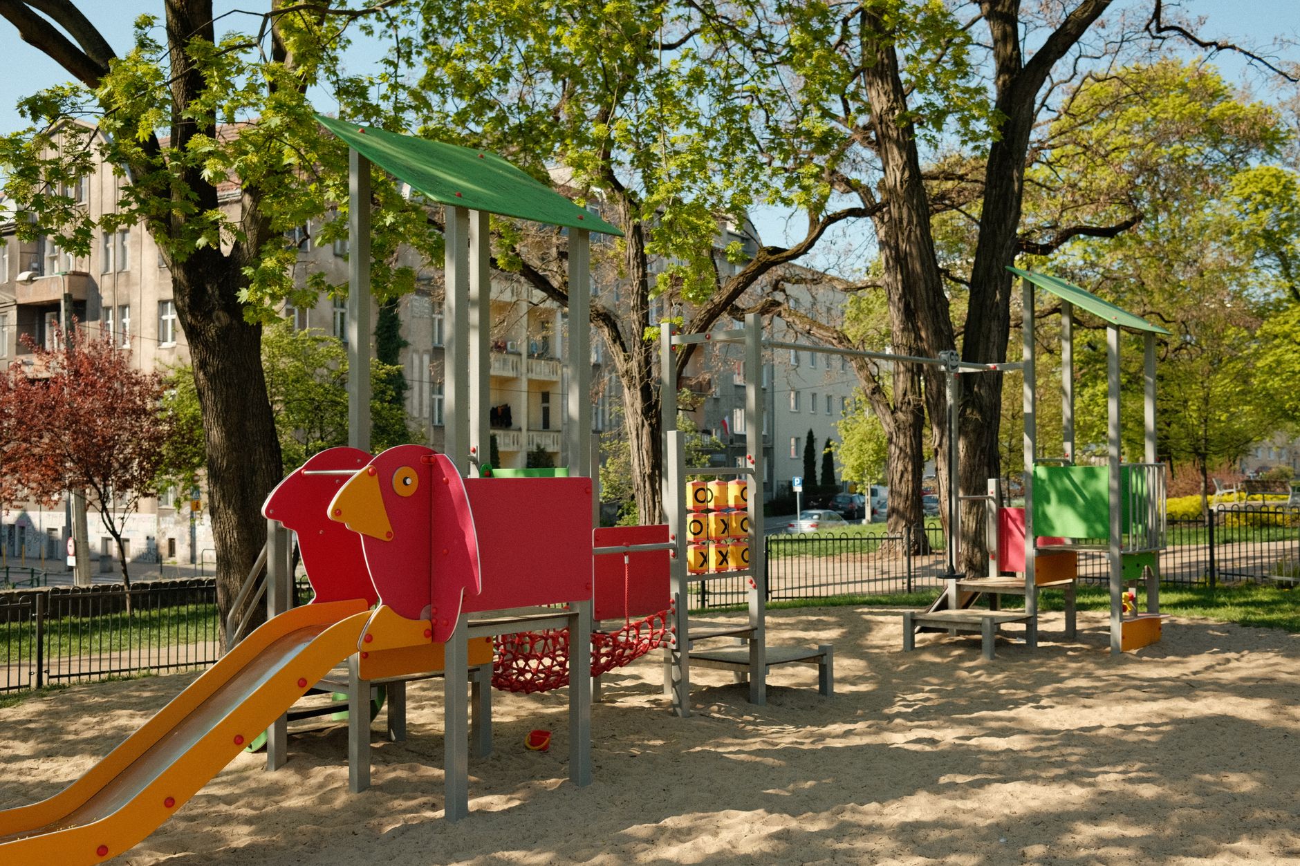 A vibrant playground surrounded by trees and residential buildings on a sunny summer day.