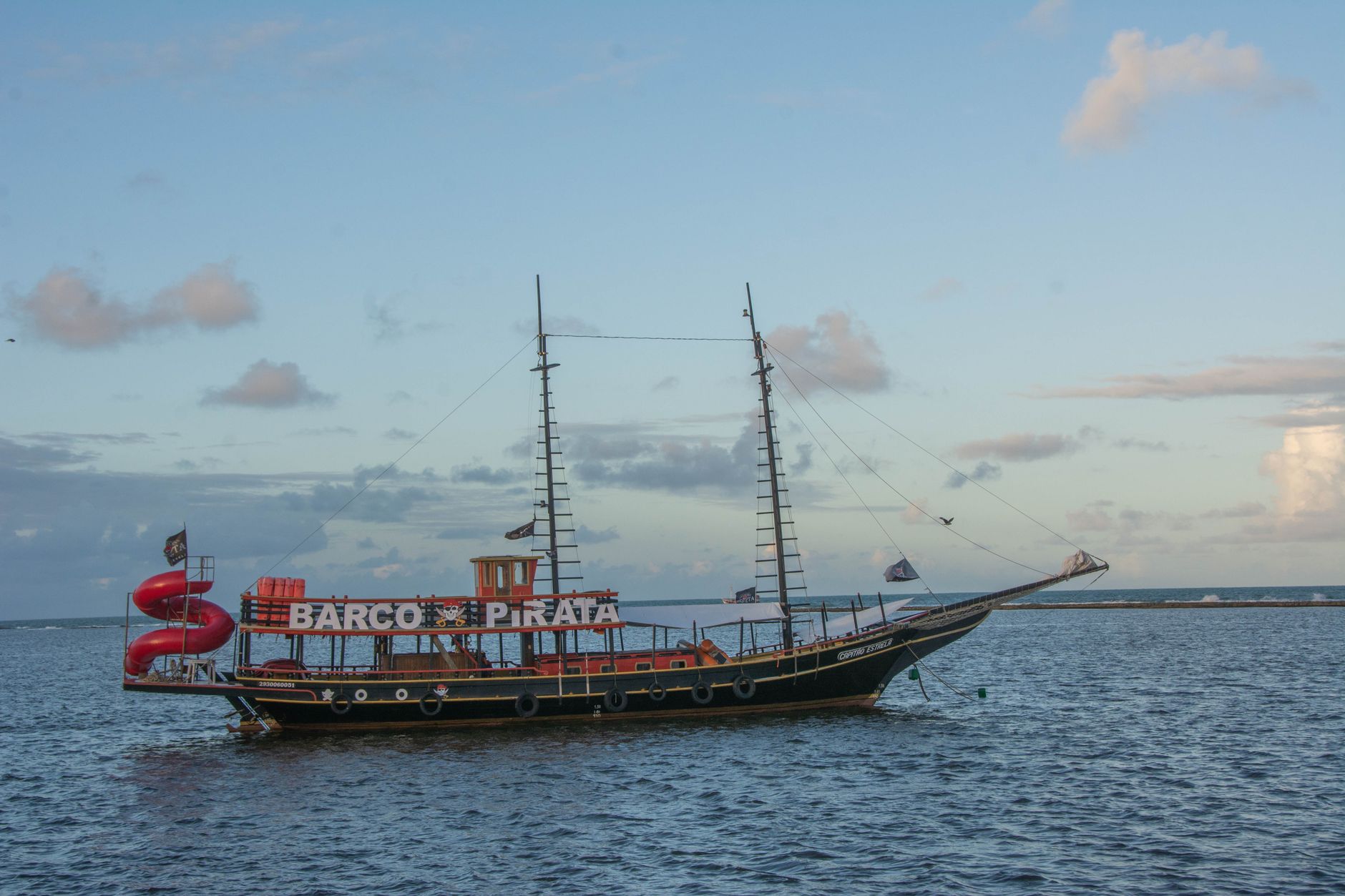 A colorful pirate ship sails on the waters of Porto Seguro, Bahia, Brazil, under a bright sky.