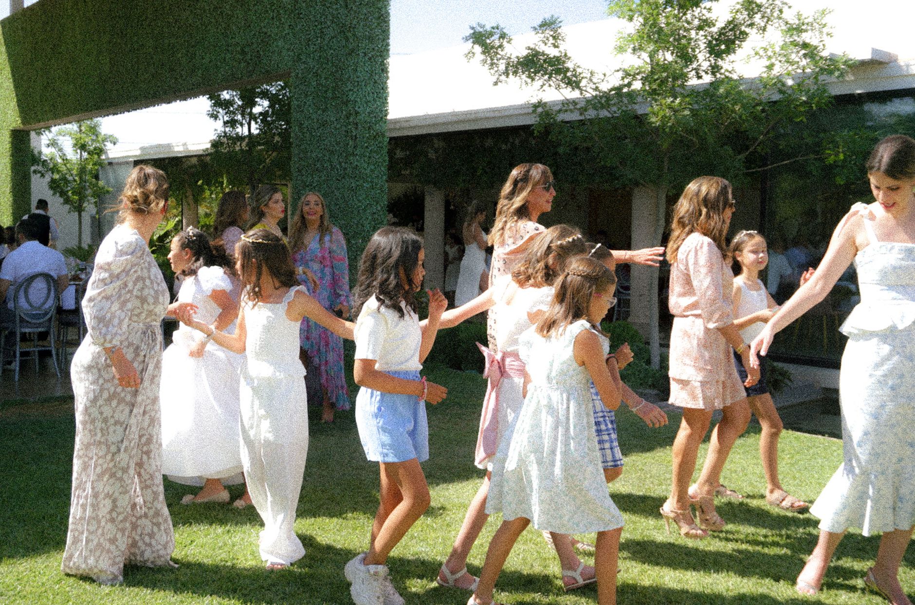 Joyful children playing together outdoors at a summer garden party with parents nearby.