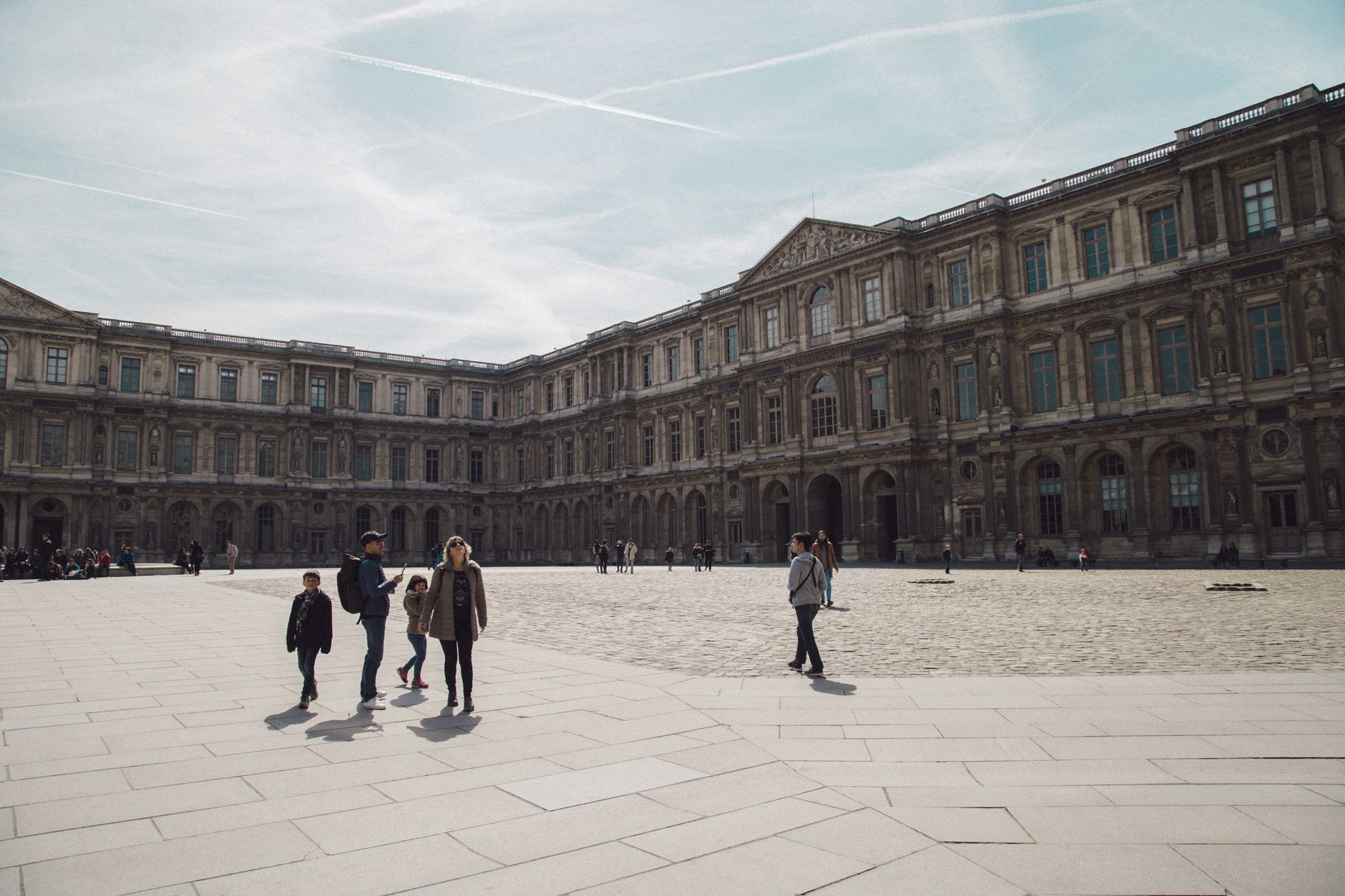 Tourists stroll in the courtyard of the historic Louvre Museum in Paris, a famous travel destination.