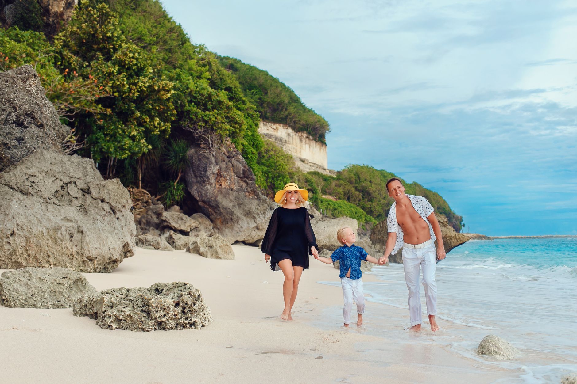 Family enjoying a sunny day walking on a picturesque beach in Bali, Indonesia.