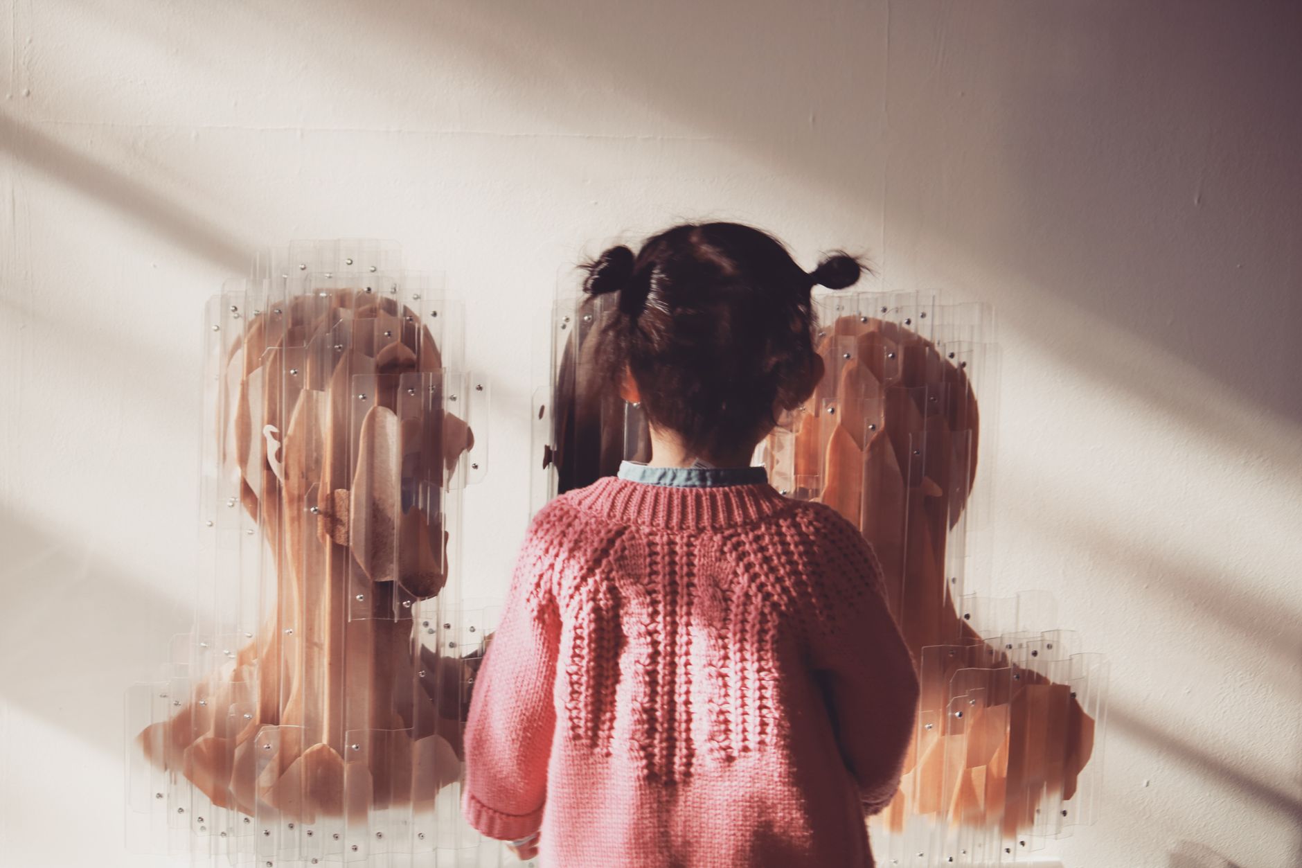 Back view of anonymous little girl with bunches in warm clothes standing in front of paintings in modern museum