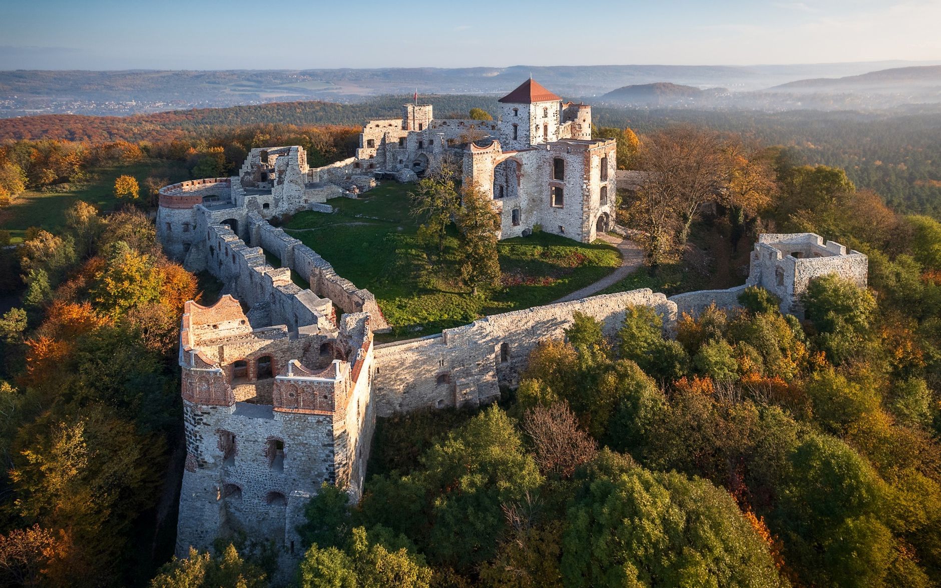 Aerial view of the medieval Tenczyn Castle amidst vibrant autumn foliage in Poland.