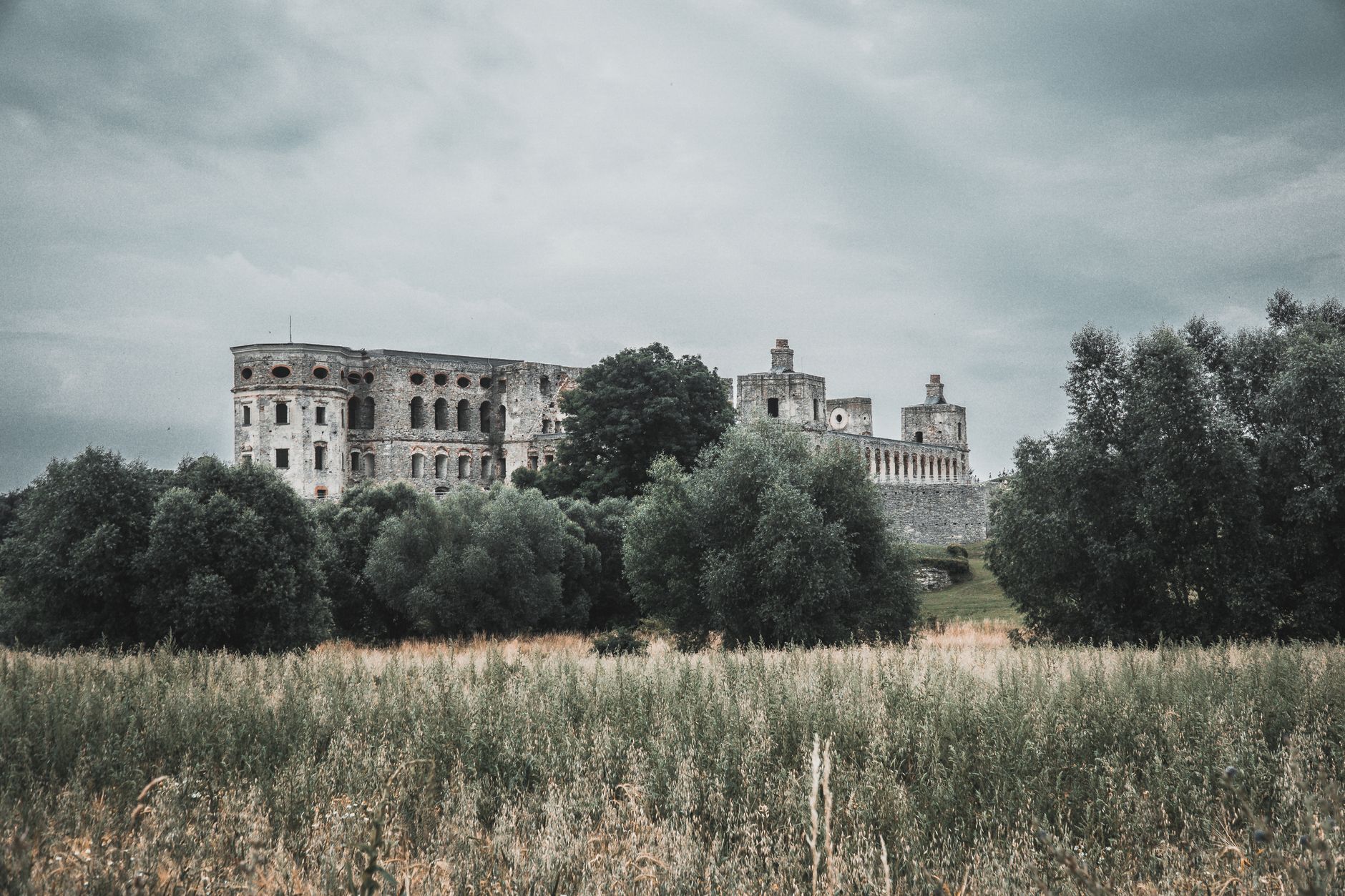 Scenic view of a Renaissance castle in Poland surrounded by lush greenery and fields under an overcast sky.