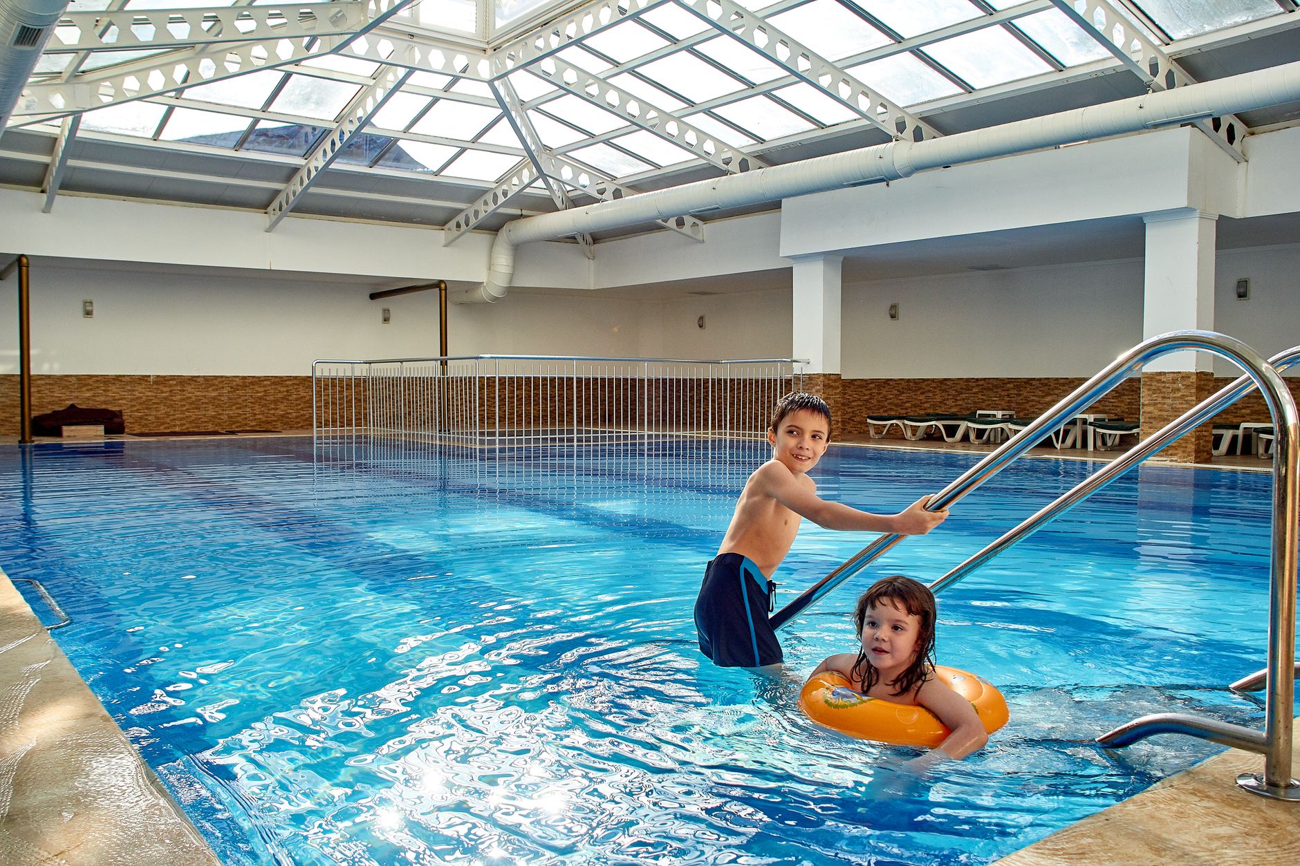 Two children playing in an indoor swimming pool, having a fun time.