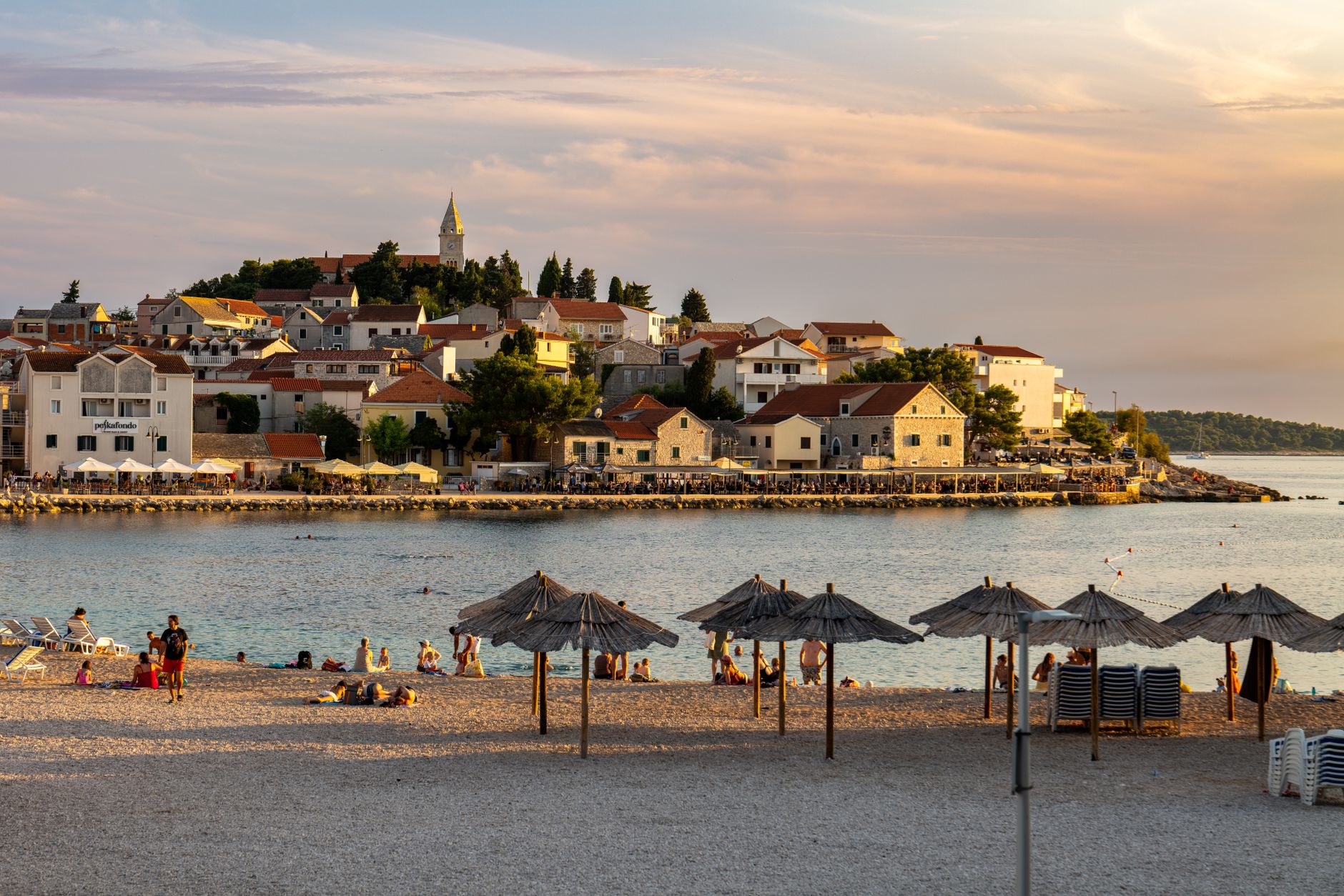 Beautiful beach scene with town and umbrellas at sunset in Primošten, Croatia.