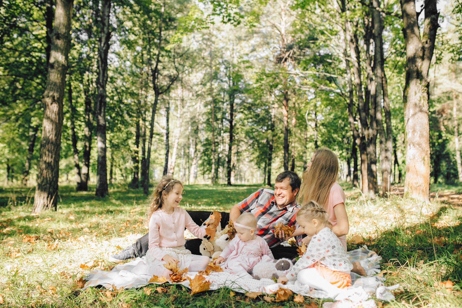 A joyful family picnic with parents and children surrounded by green trees and sunshine.