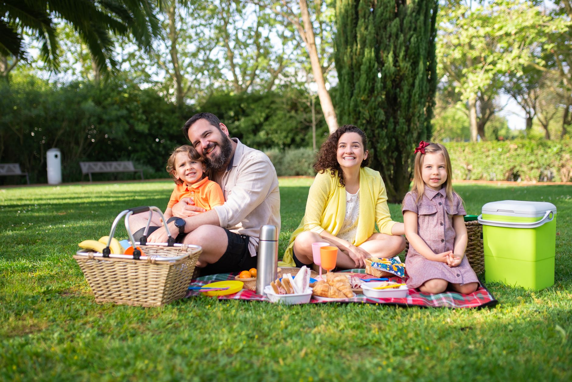 Happy family having a picnic at a sunny park, sitting on a blanket with food, laughing and enjoying together time.