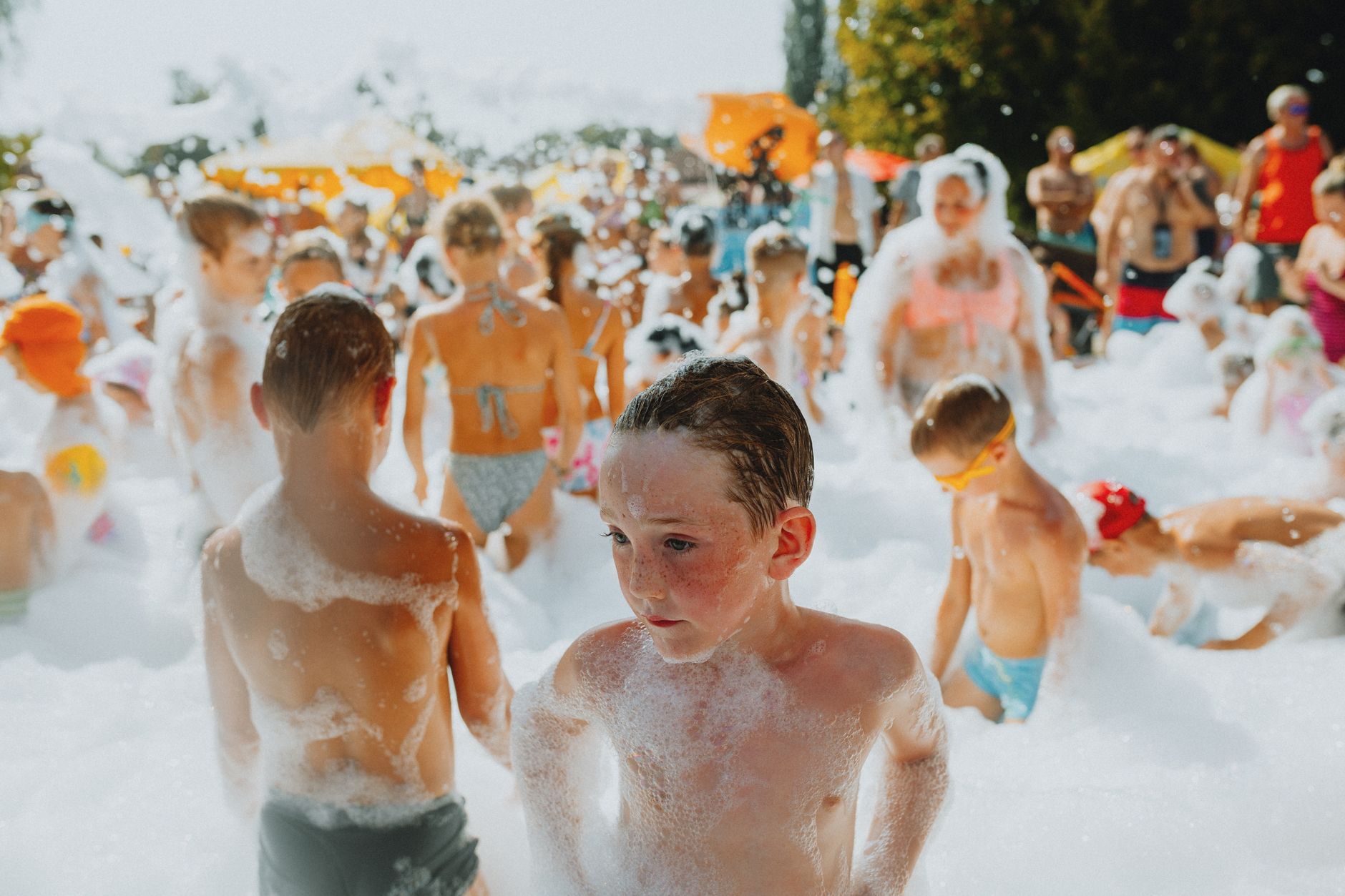 A cheerful group of children playing in a lively outdoor foam party on a sunny day.